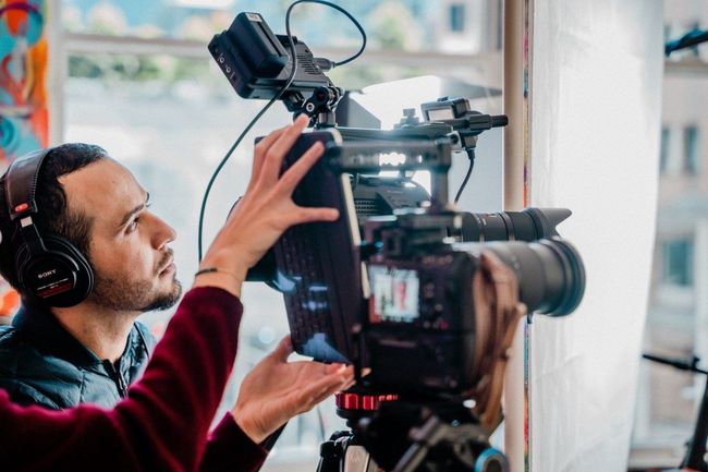 Cameraman adjusting a professional video camera on a tripod near a window
