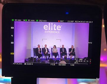 Panel discussion on an Elite Experience stage with five speakers seated under purple lighting