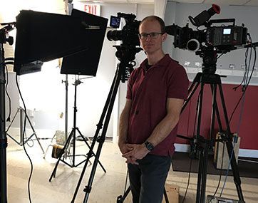 Person standing in a photo studio with cameras, tripods, and large softbox lights.