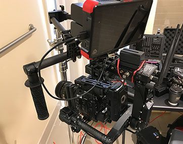 Professional video camera rig with monitor and cables mounted on a tripod indoors