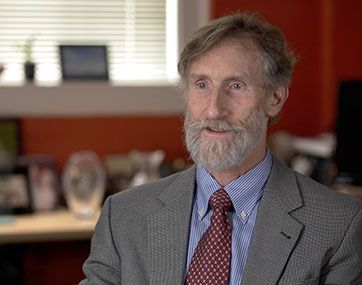 Portrait of a bearded man in a suit and tie, seated in an office setting