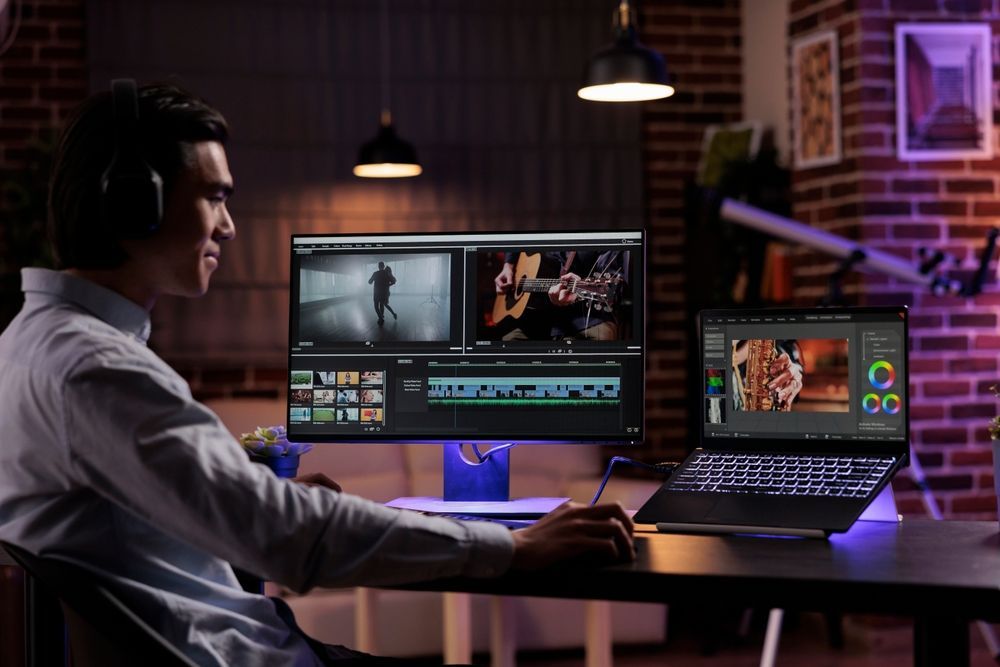 Person editing video on dual monitors in a dim studio with purple lighting
