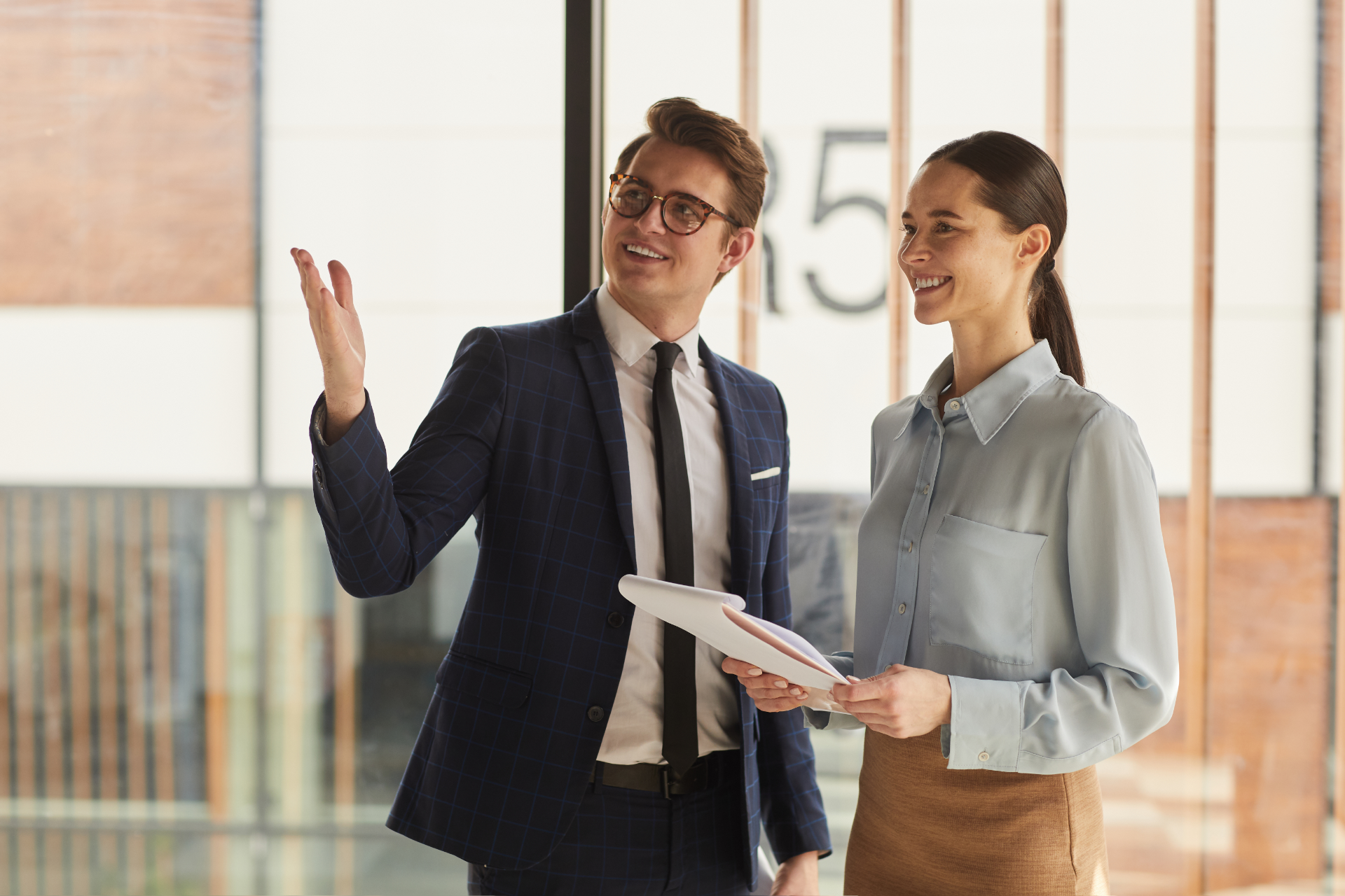 Couple in a convertible car, smiling while driving through a green, wooded area on a sunny day.