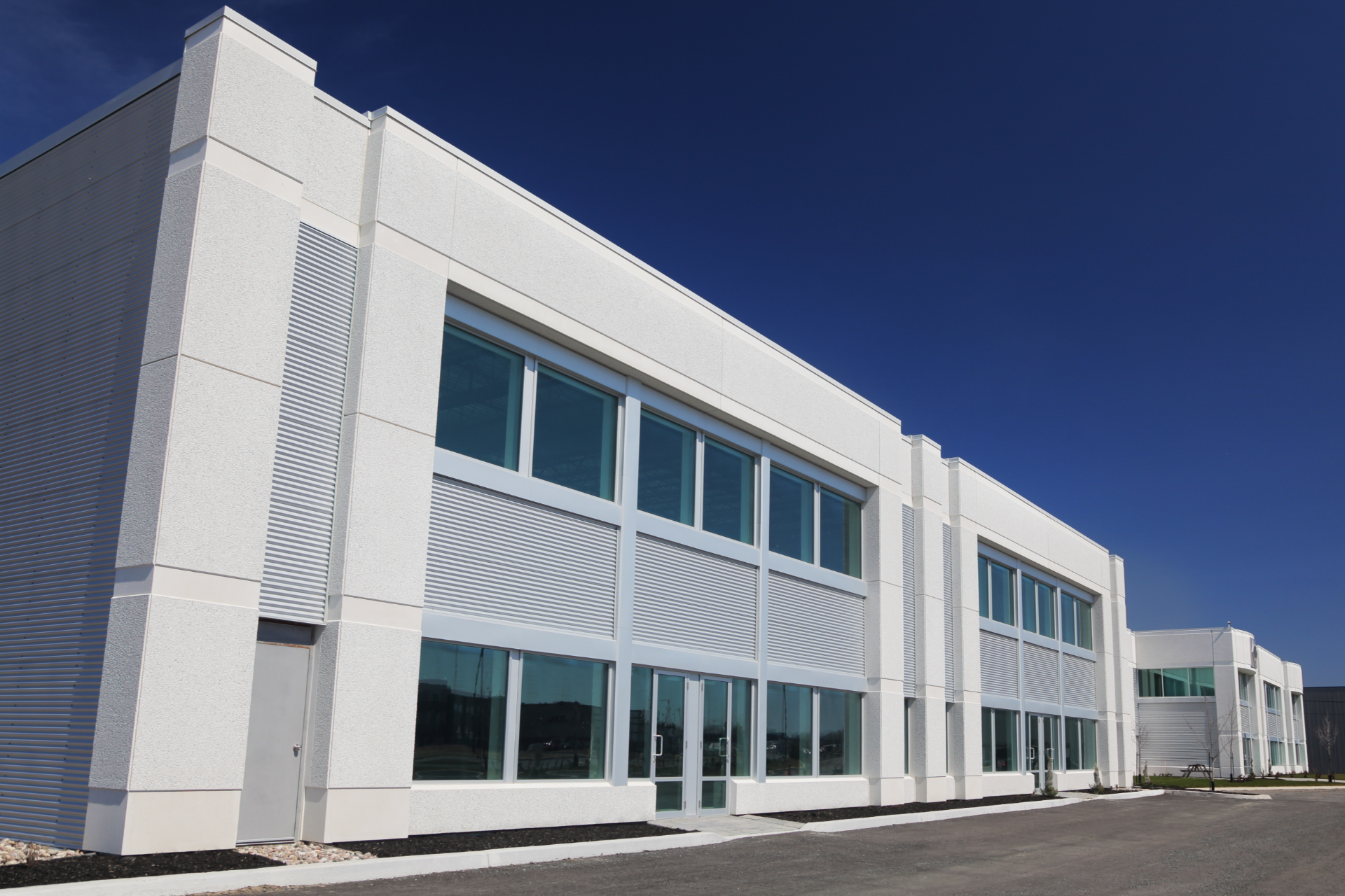 A modern, white, two-story commercial office building with large glass windows under a clear blue sky.