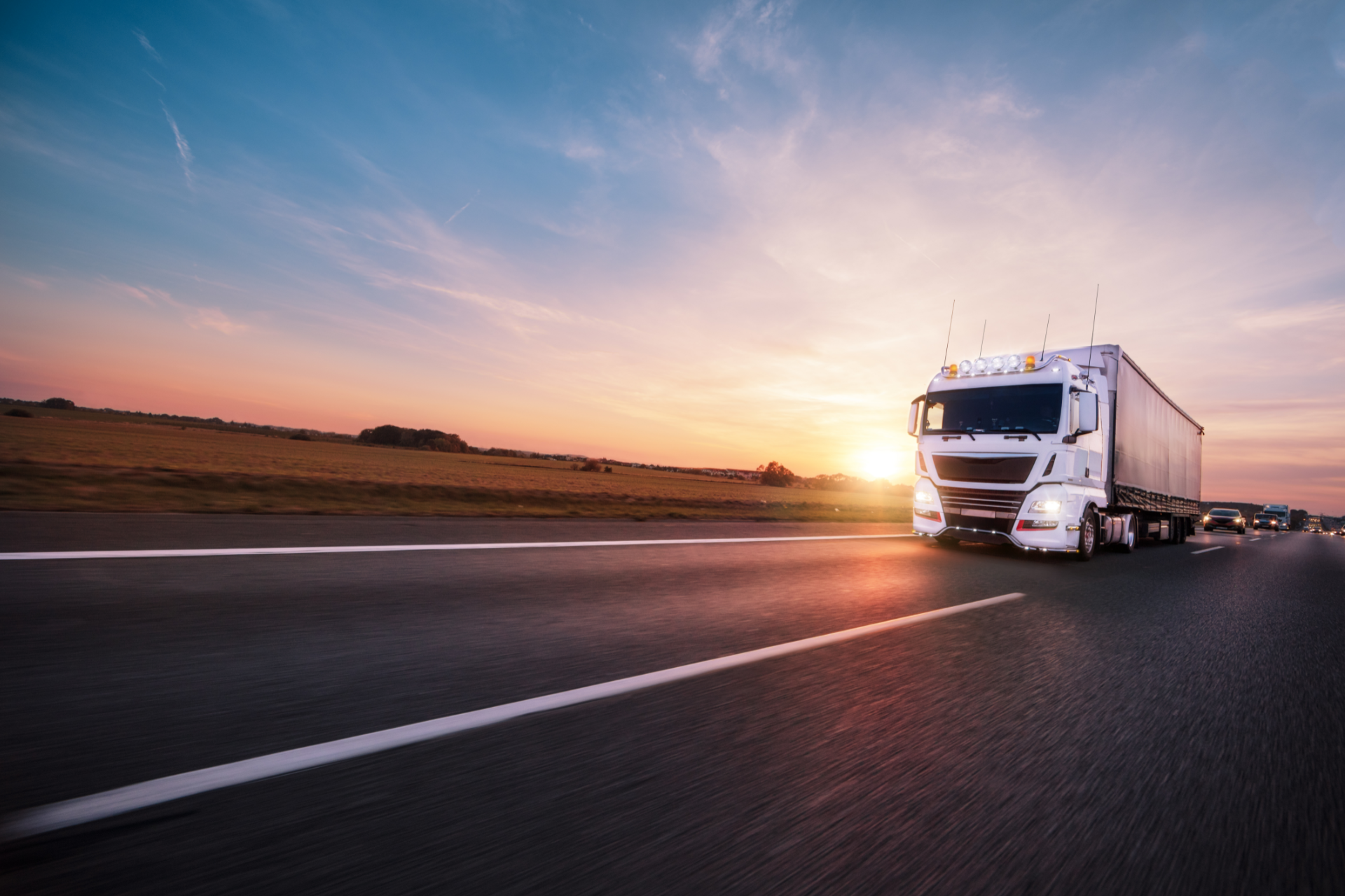 A white semi-truck driving on a highway at sunset.