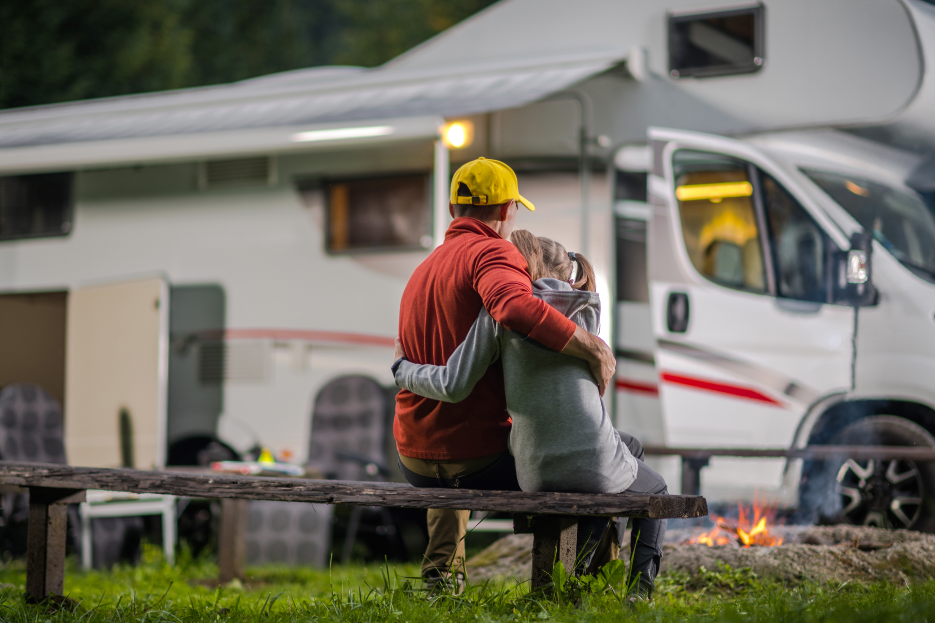 Couple in a convertible car, smiling while driving through a green, wooded area on a sunny day.