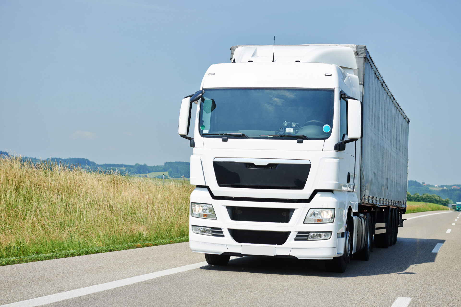 Couple in a convertible car, smiling while driving through a green, wooded area on a sunny day.