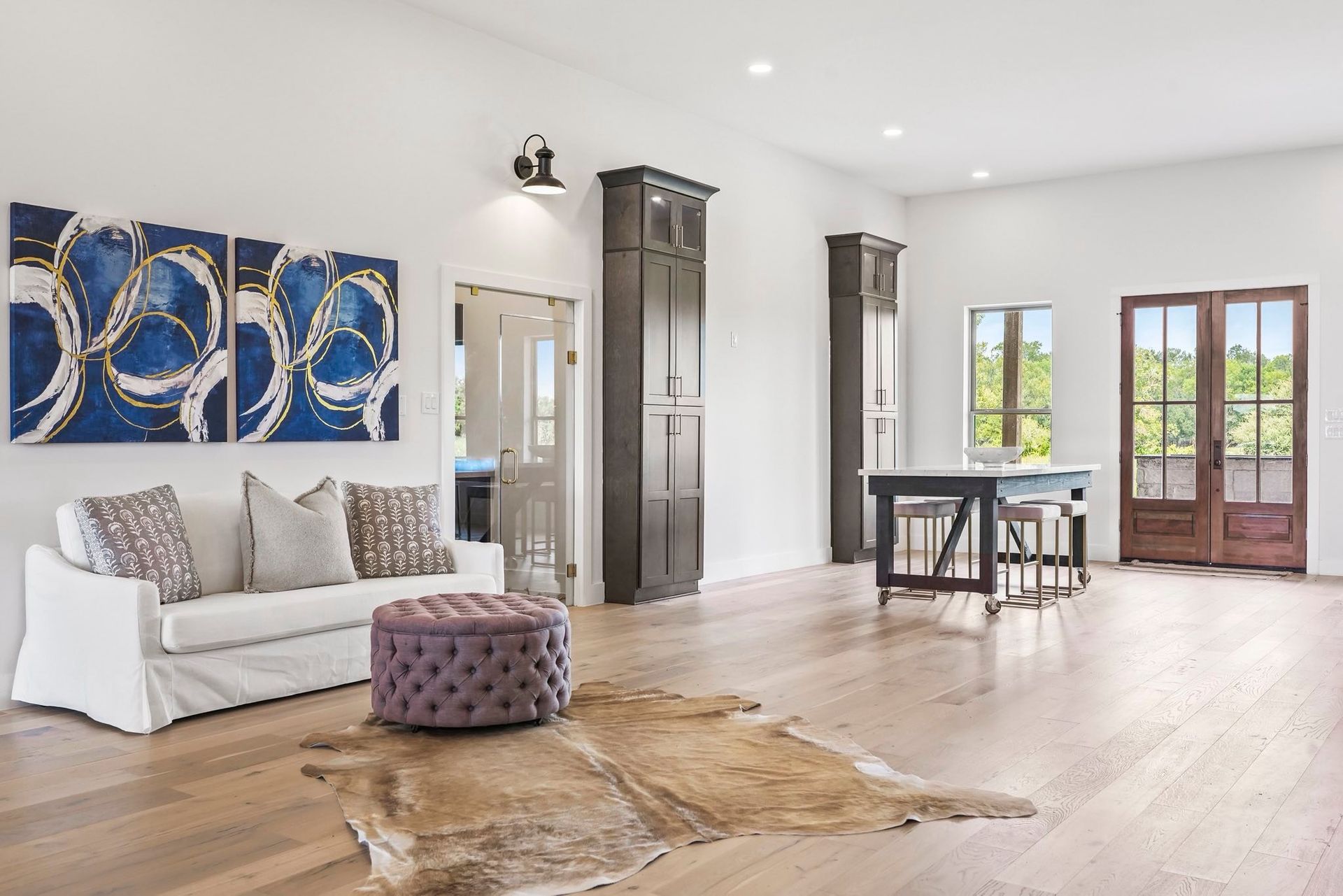 Spacious room with hardwood floors, white walls, and a blue and gold triptych above a white sofa.