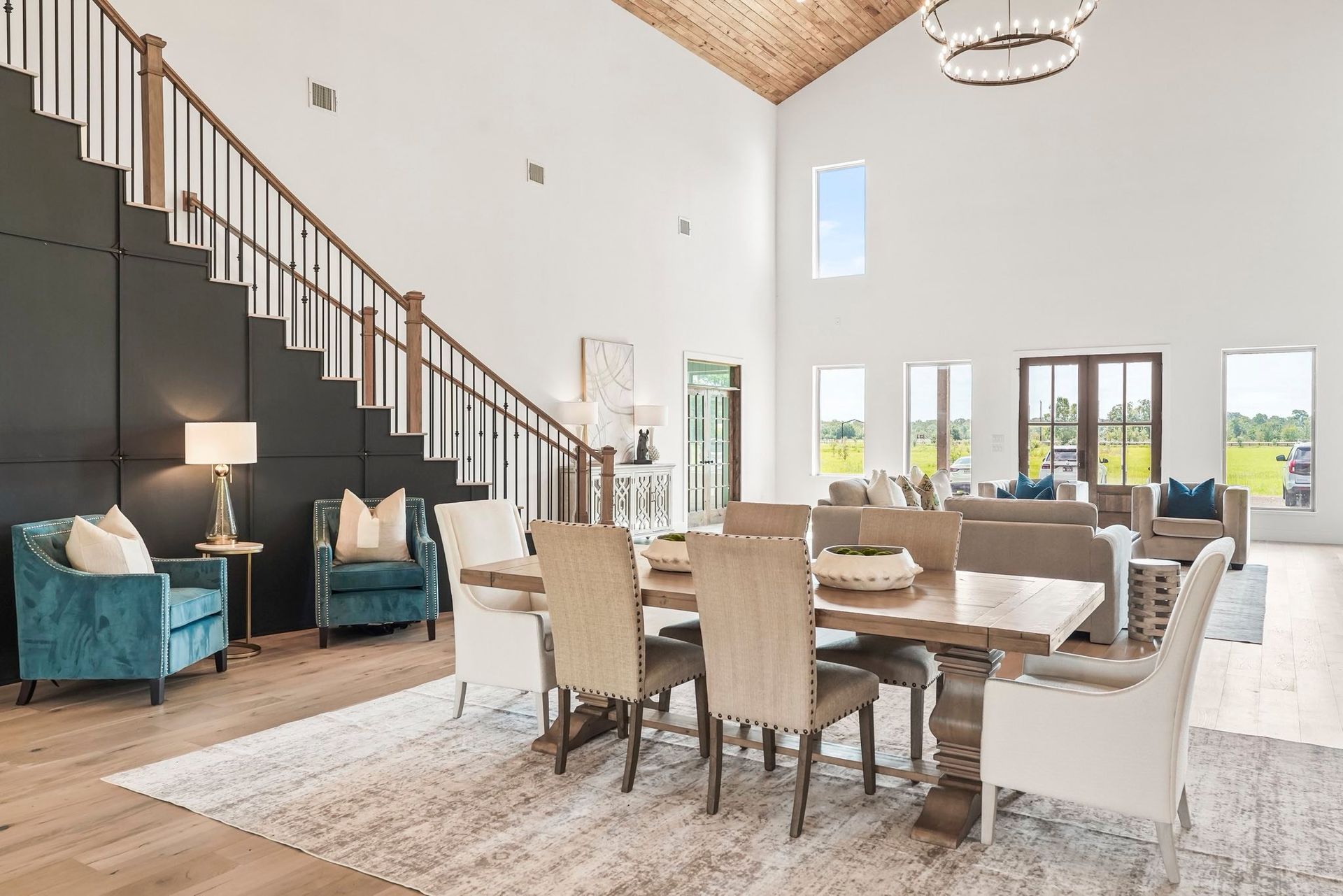 Spacious dining and living area with high ceilings, featuring a table, chairs, and two teal armchairs.