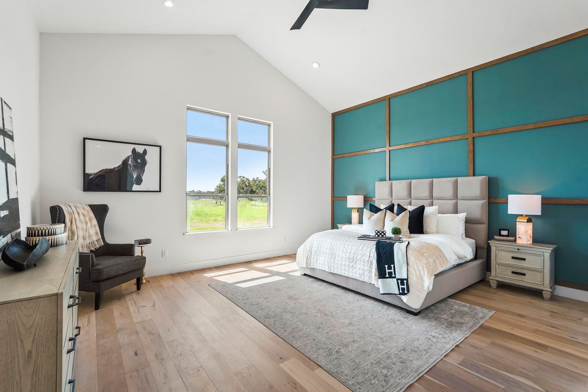 Spacious bedroom with teal accent wall, king bed, arm chair, and a view of the outdoors.