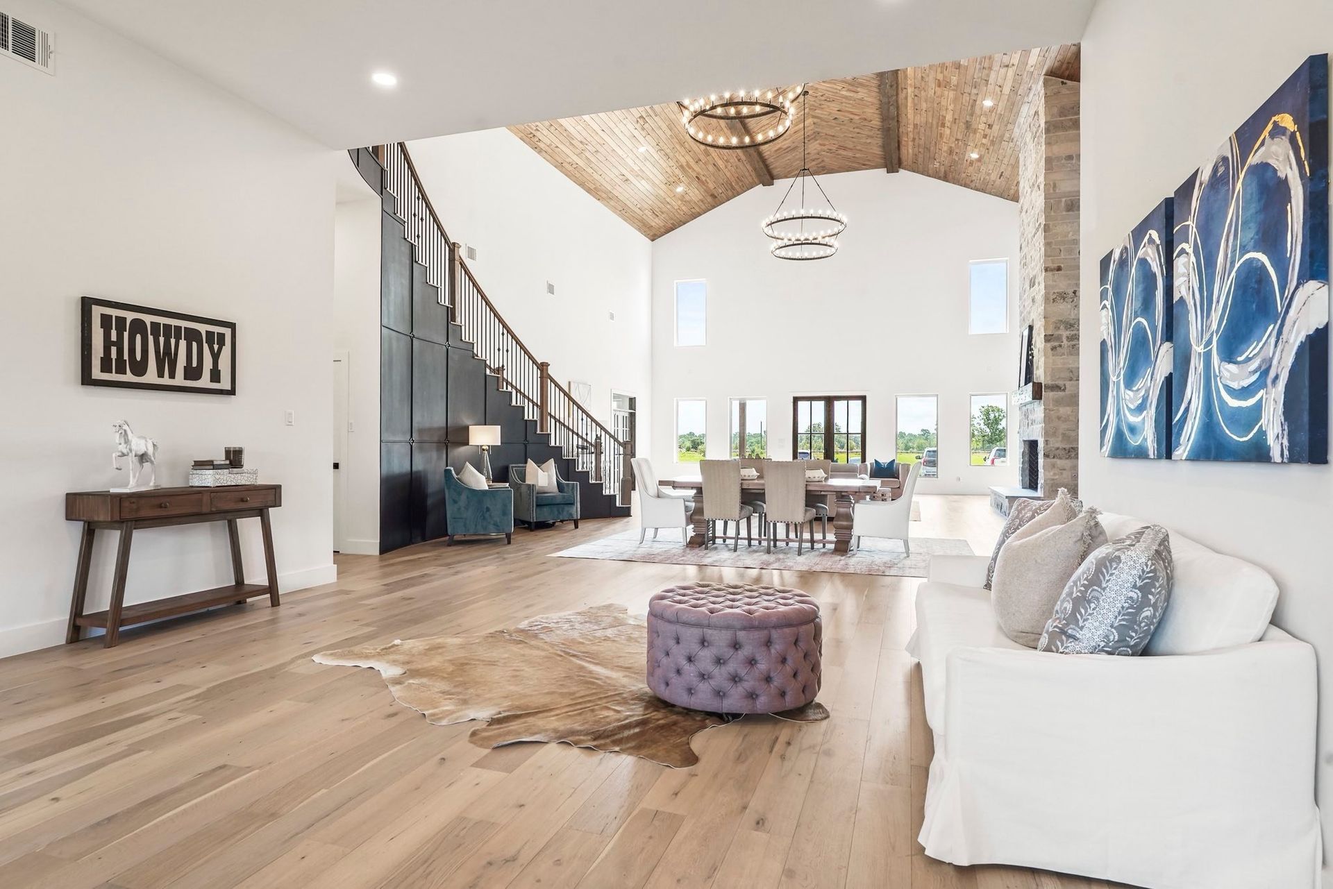 Spacious living room with wood floors, a staircase, and a dining area, featuring a cowhide rug and artwork.
