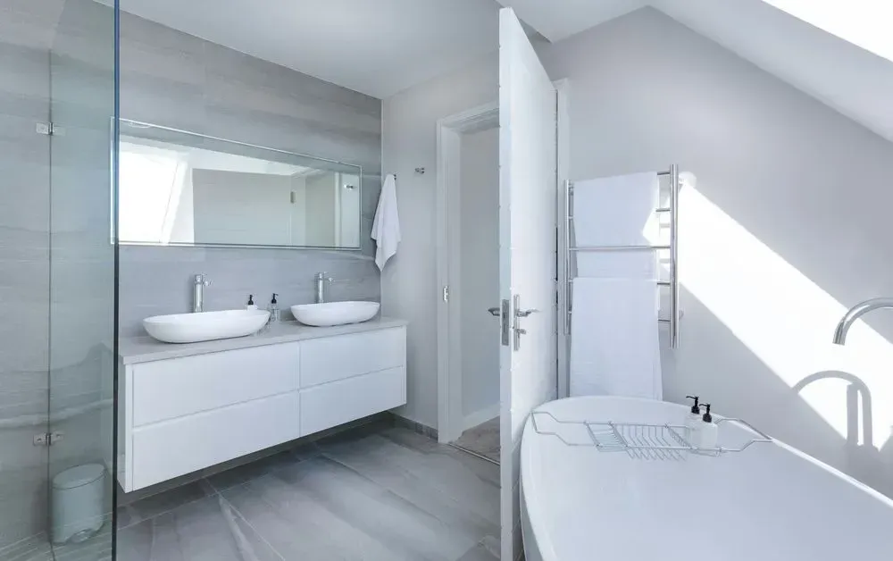 Bright modern bathroom with double sinks, glass shower, and a freestanding tub by a skylight.