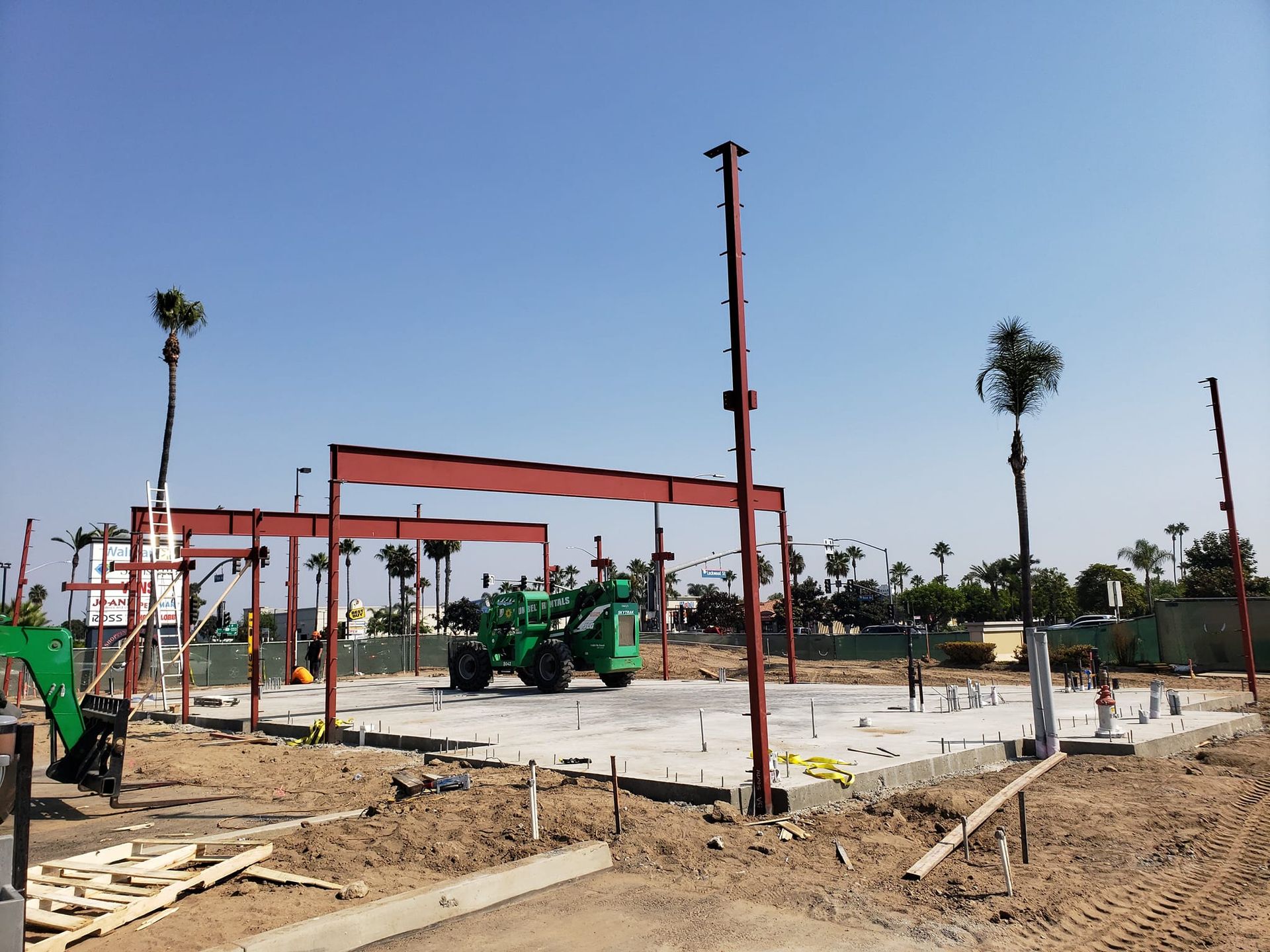 A construction site with a green tractor and palm trees