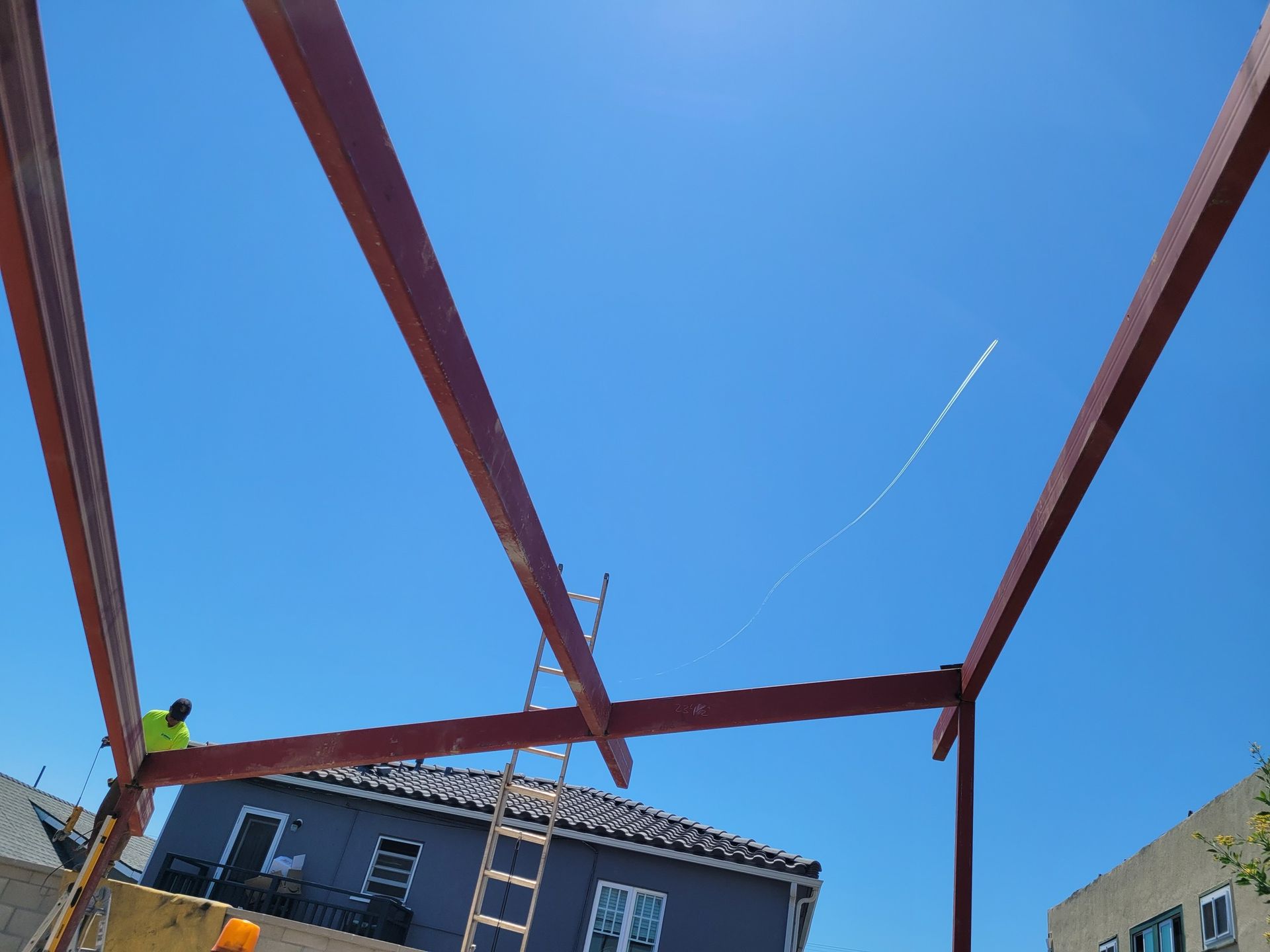 A man is standing on a ladder in front of a building under construction.