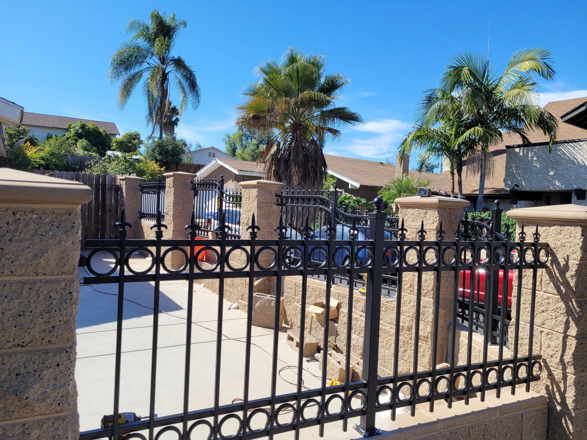 A wrought iron fence surrounds a driveway with palm trees in the background