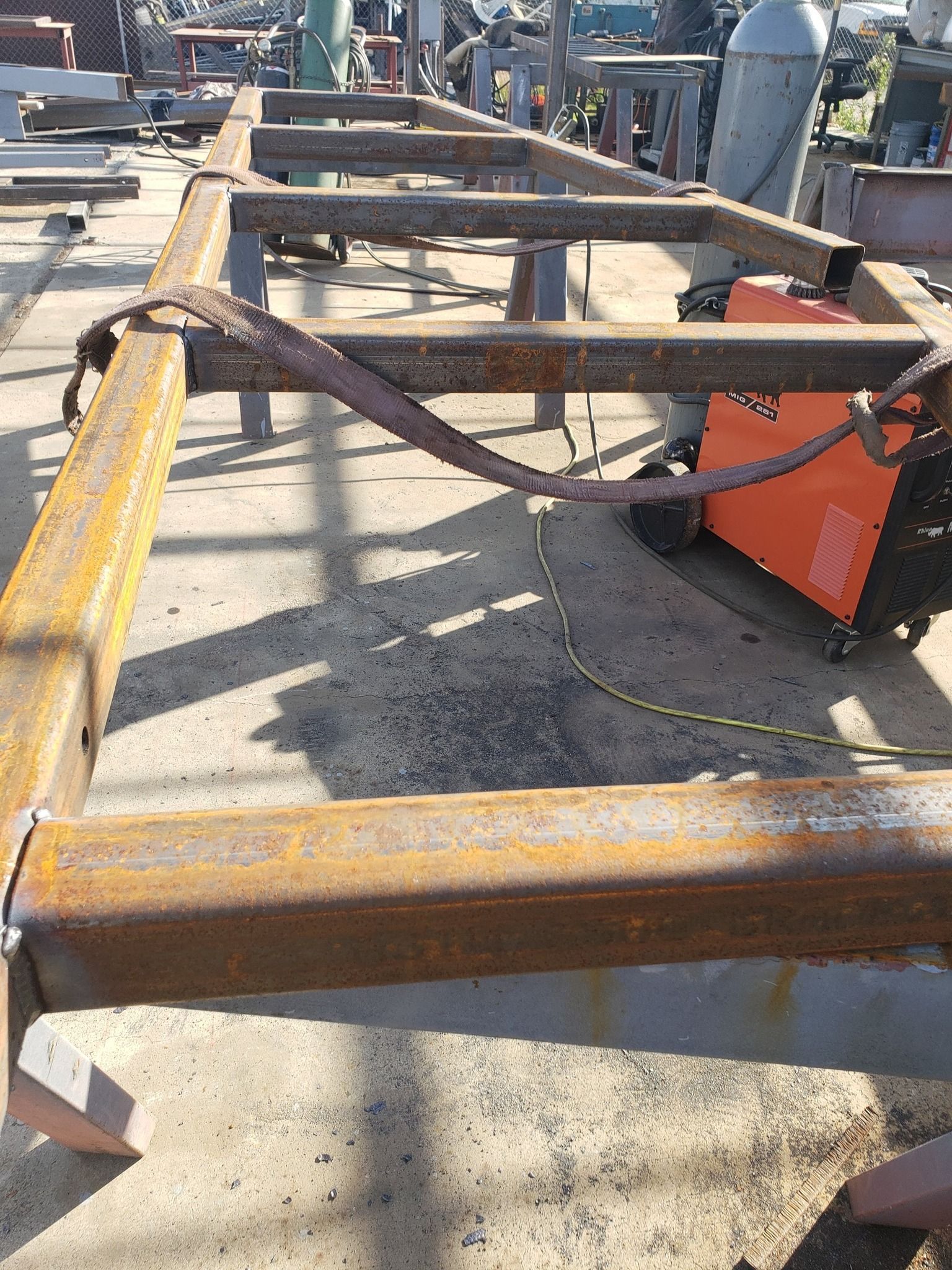 A piece of metal is sitting on the ground next to a welding machine.