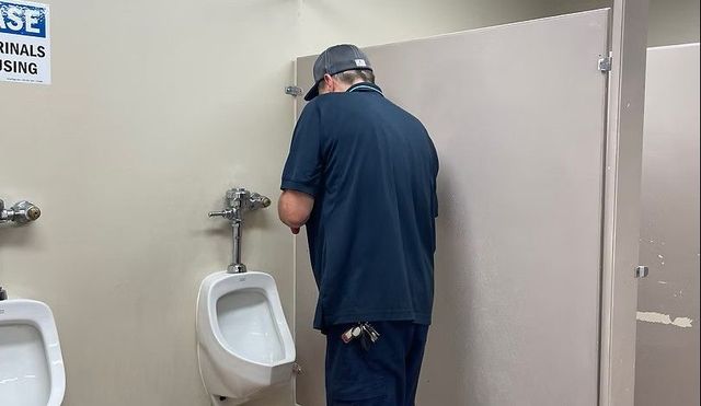 Man using urinal in public restroom.