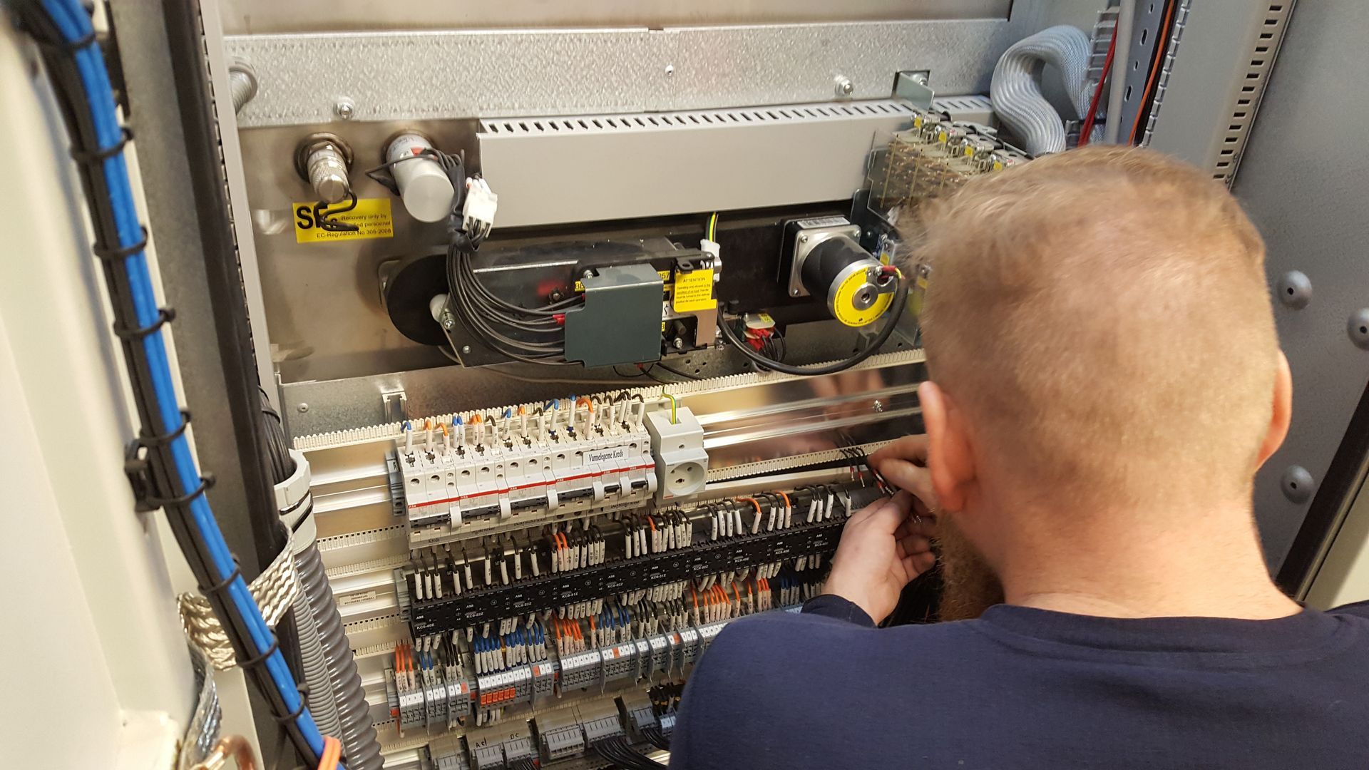 En mand arbejder på et eltavle i et rum.