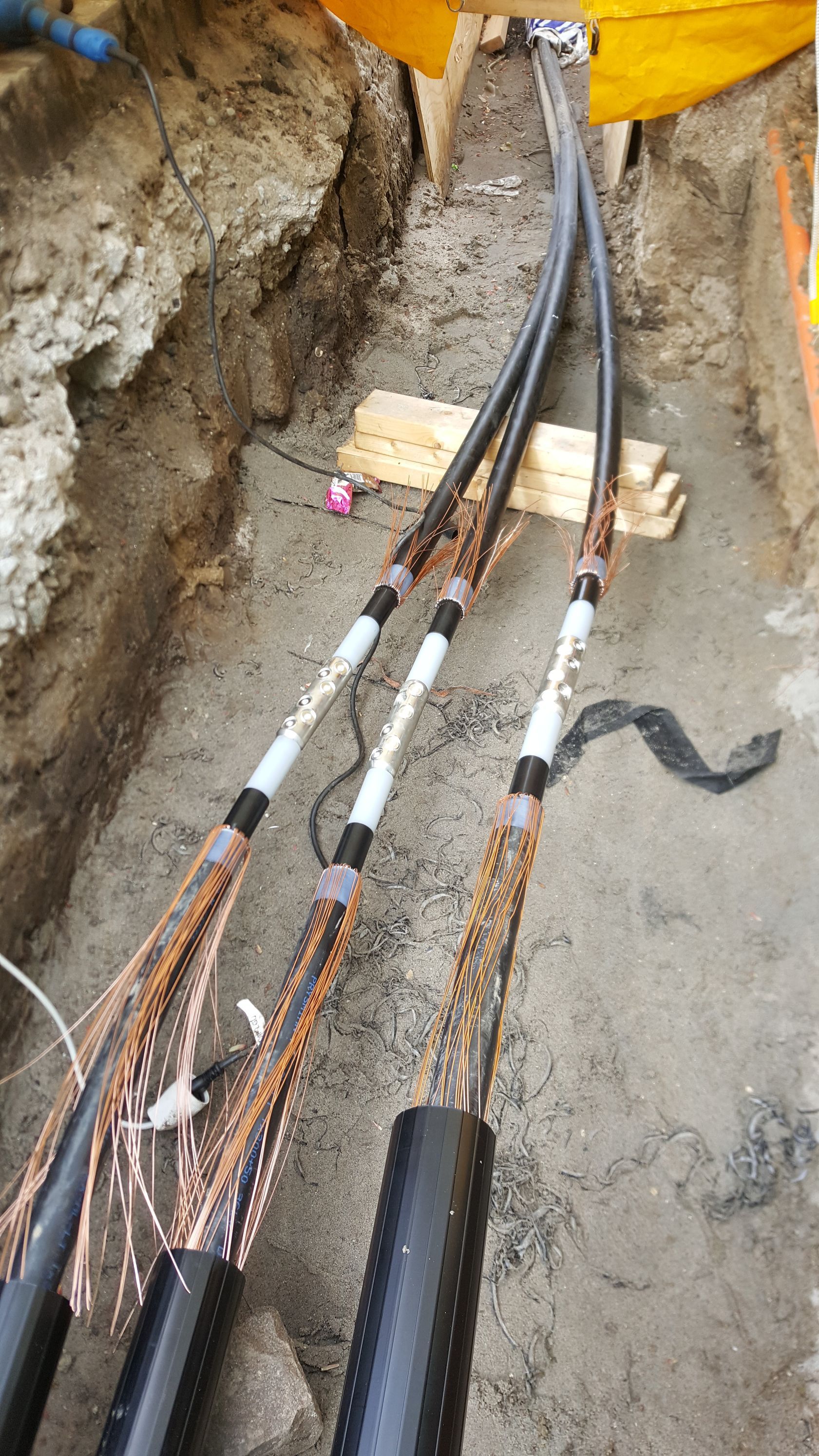 En masse ledninger ligger på jorden i en grøft.