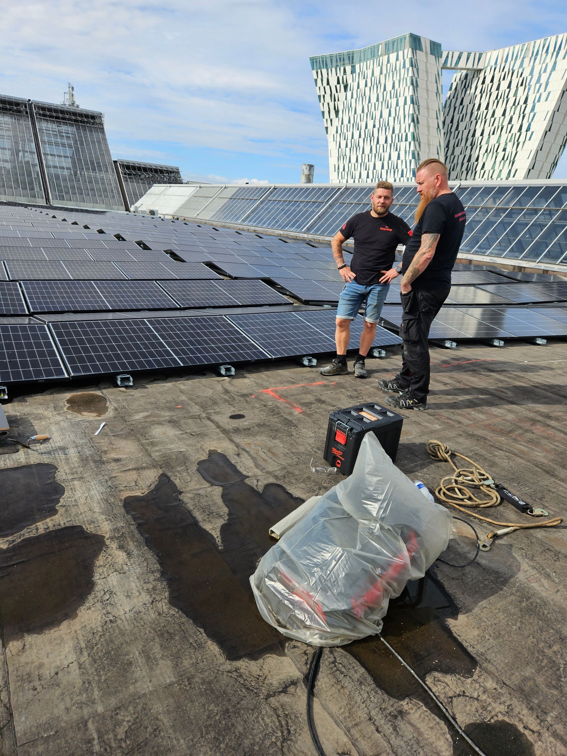 To mænd står oven på et tag med solpaneler.