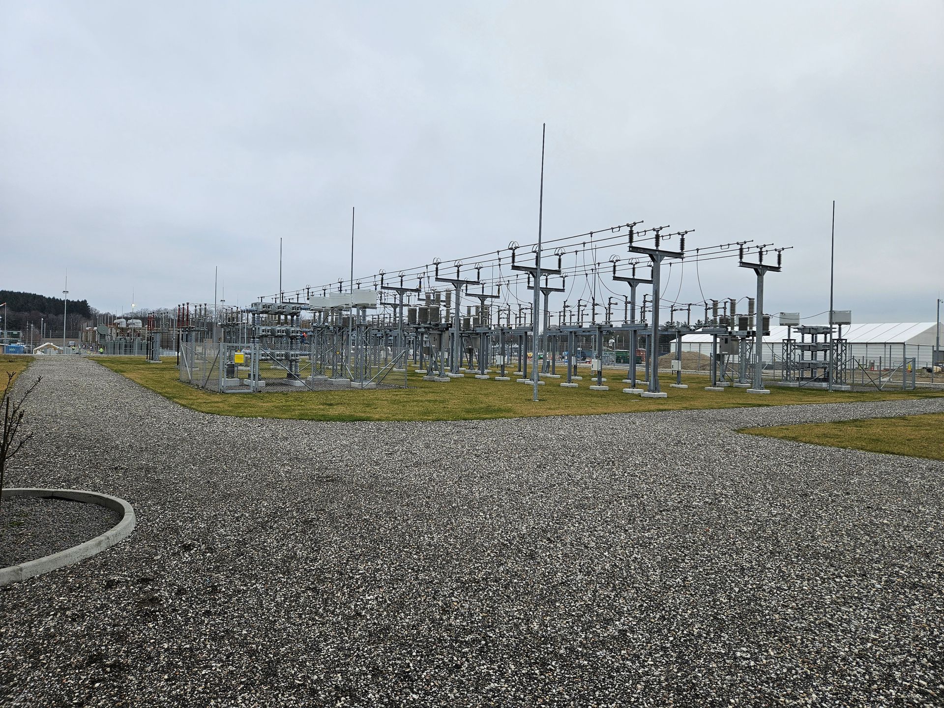 En række kraftledninger i et grusområde med en overskyet himmel i baggrunden.