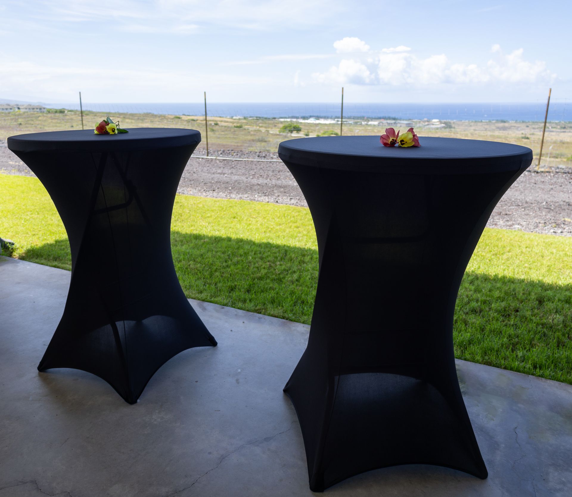 Two black tables are sitting on a patio with a view of the ocean.