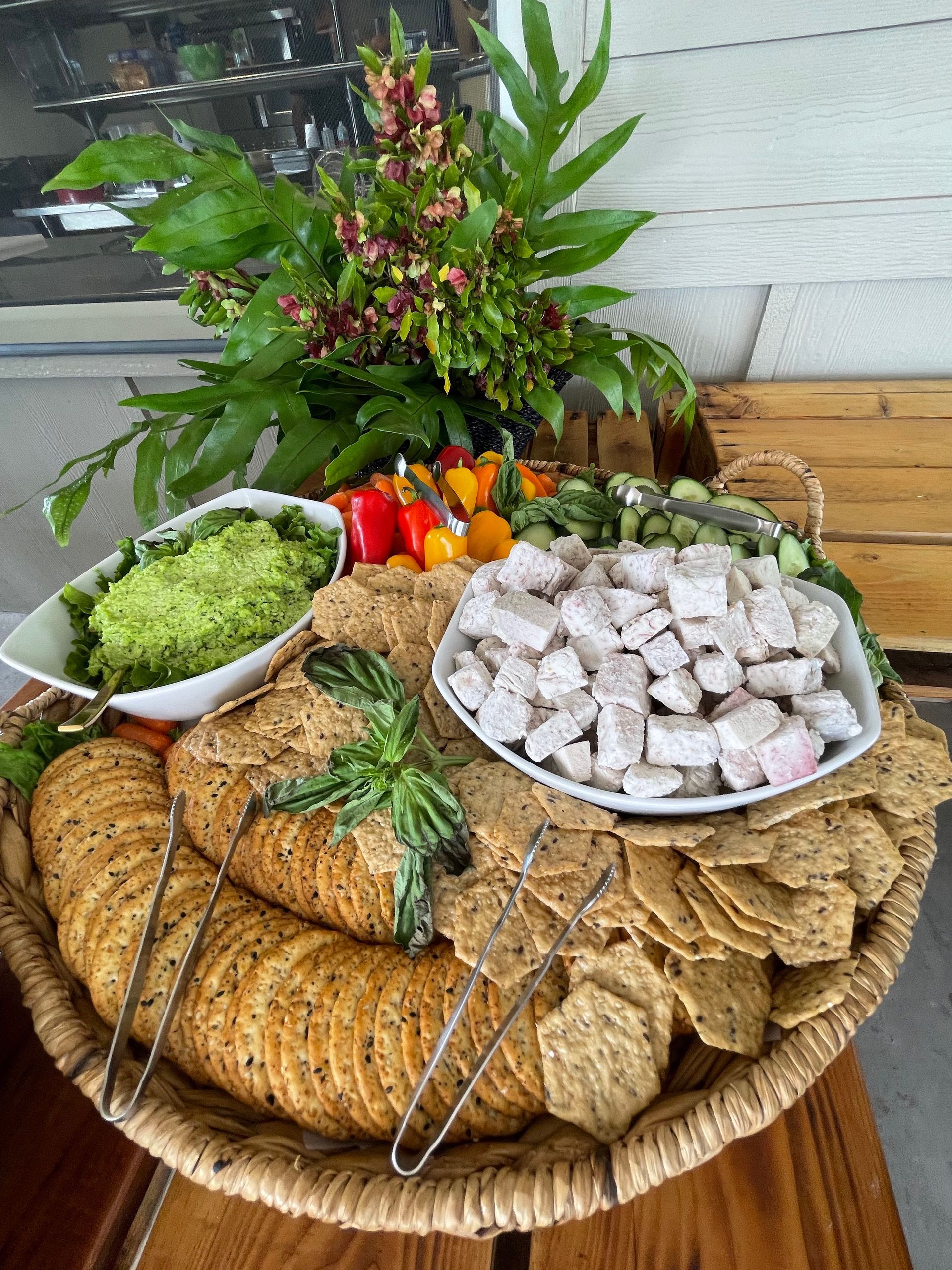 A wicker basket filled with crackers , guacamole , and vegetables on a wooden table.