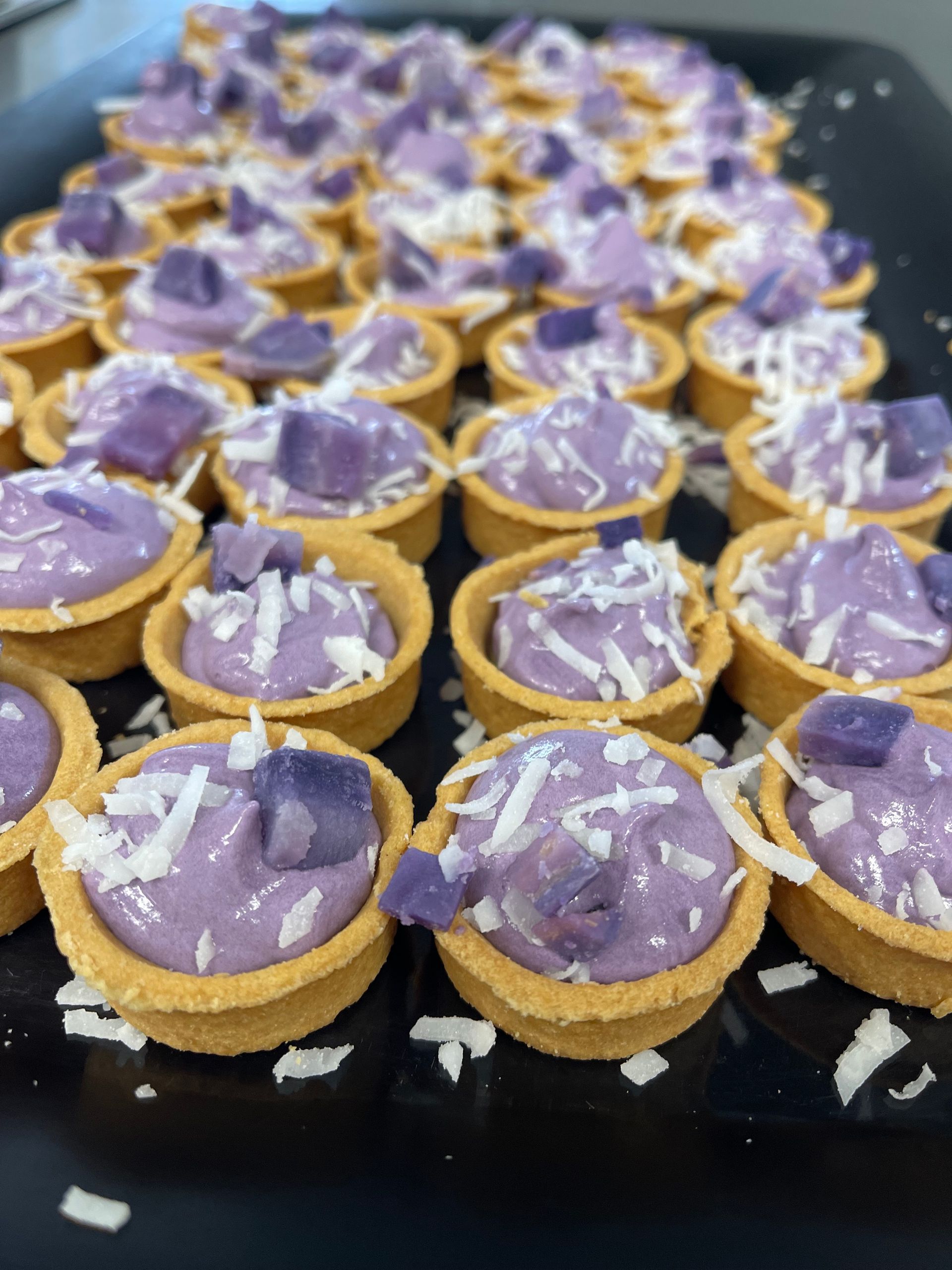 A tray of purple desserts with coconut on top