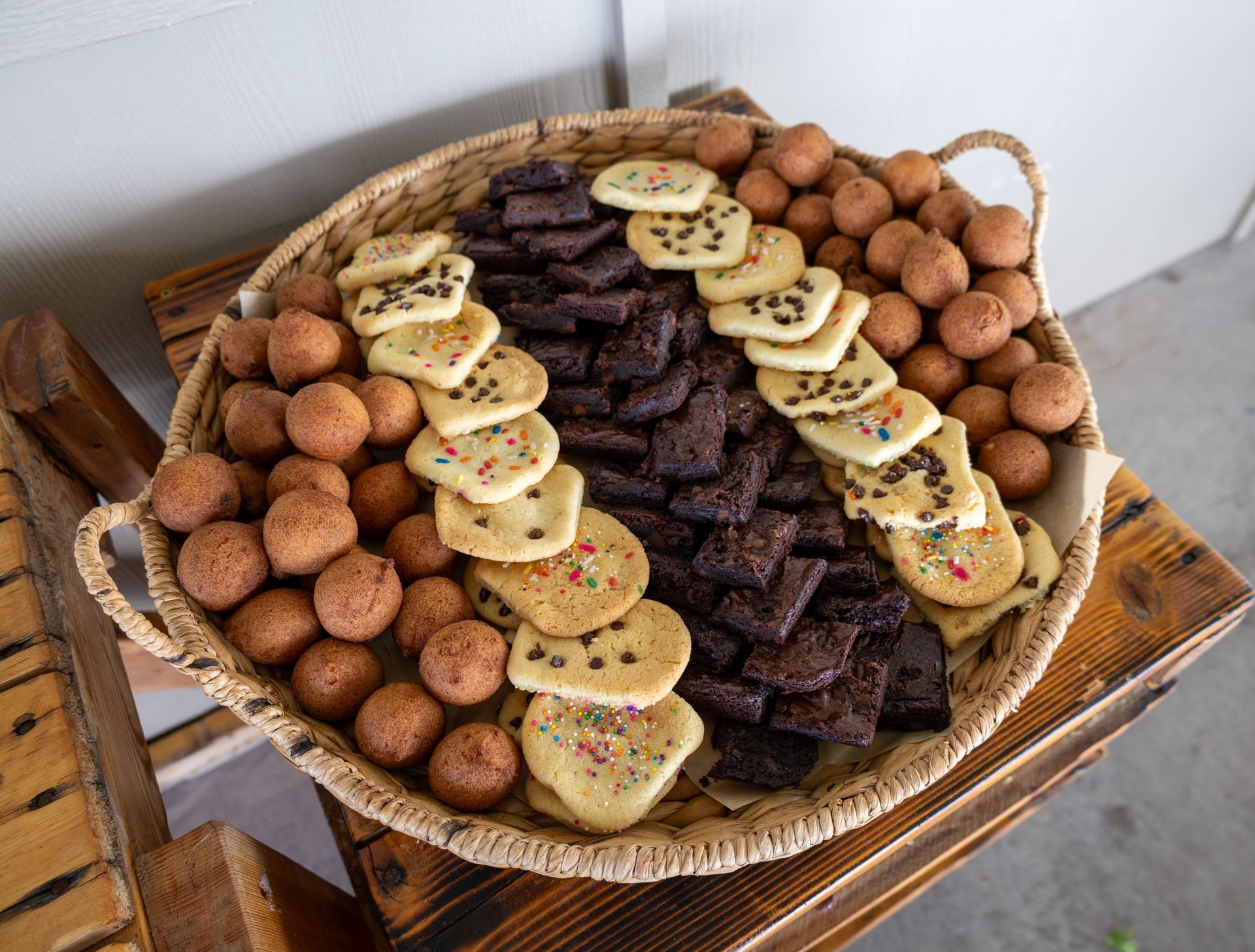 A basket filled with different types of cookies and brownies on a wooden table.