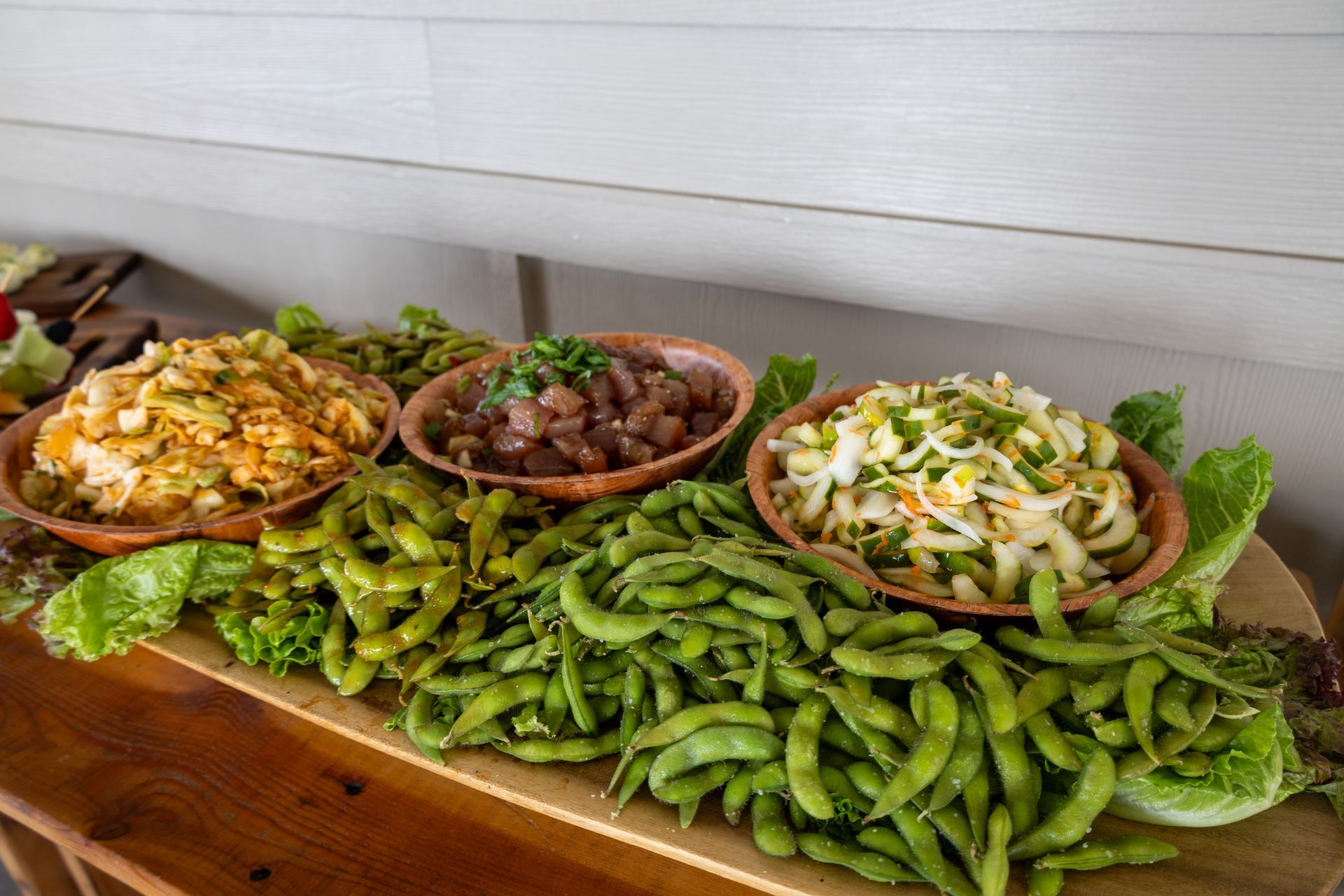 A wooden tray filled with a variety of salads and edamame beans.