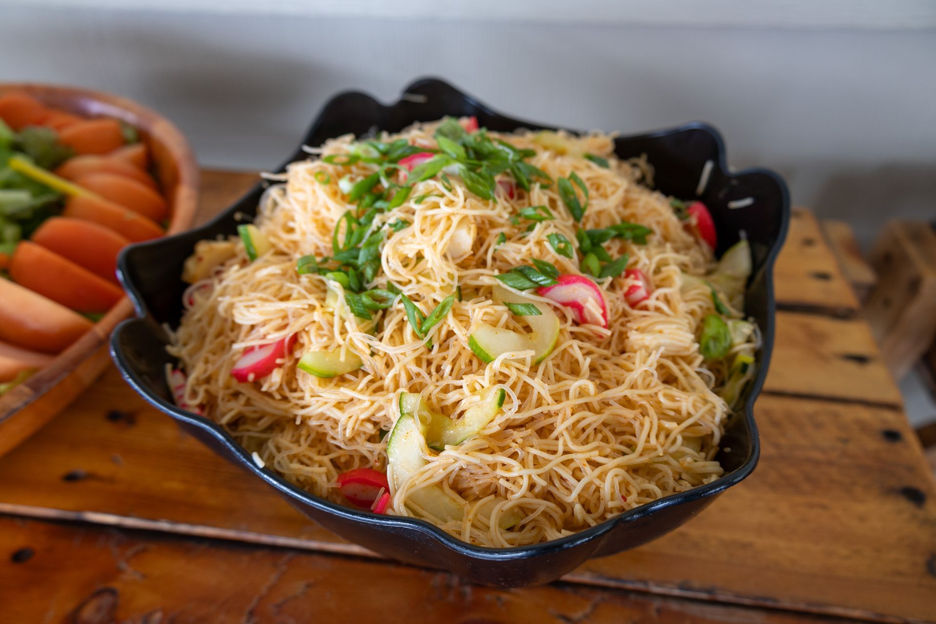 A bowl of noodles with vegetables on a wooden table.