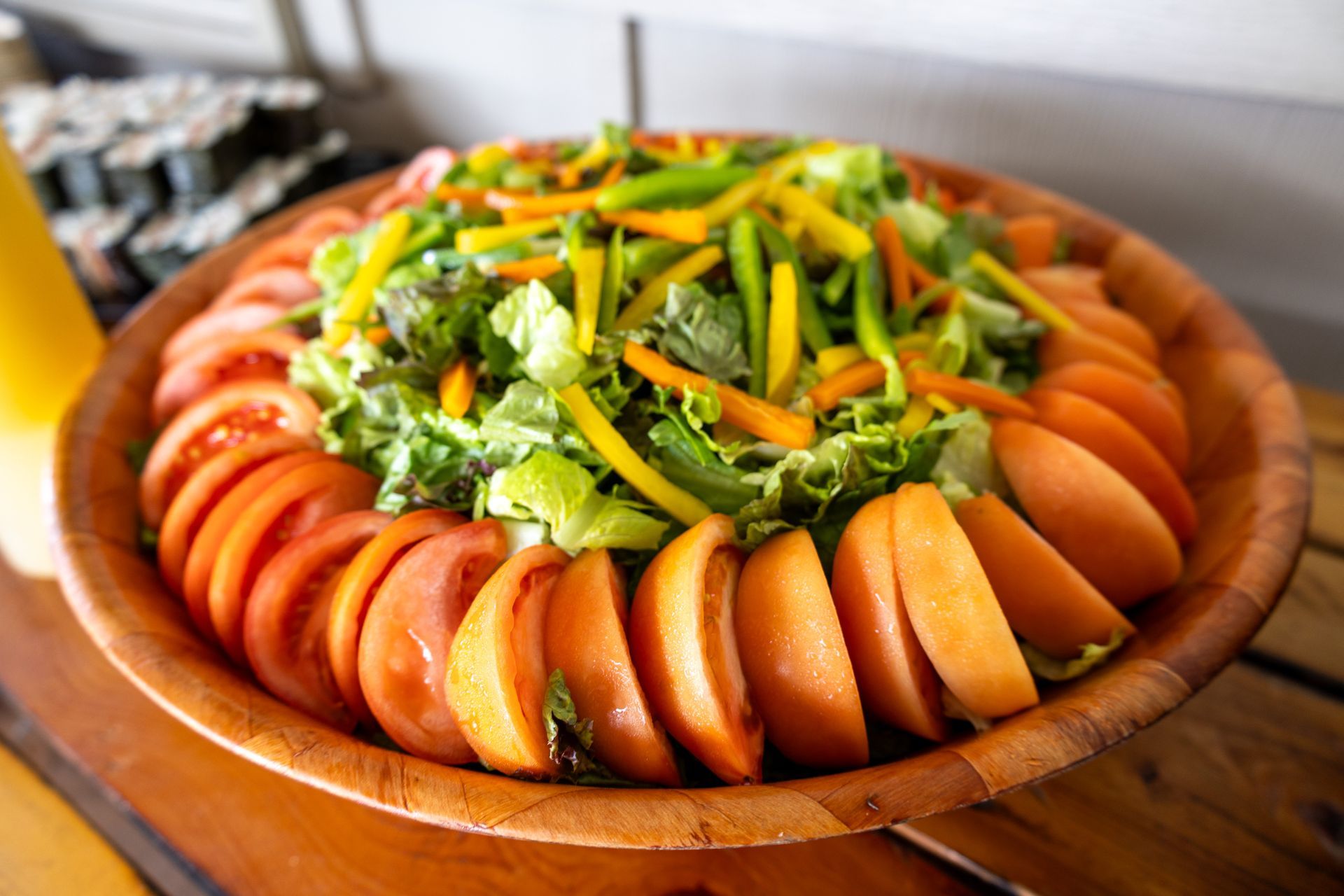 A wooden bowl filled with sliced tomatoes , carrots , lettuce and other vegetables.