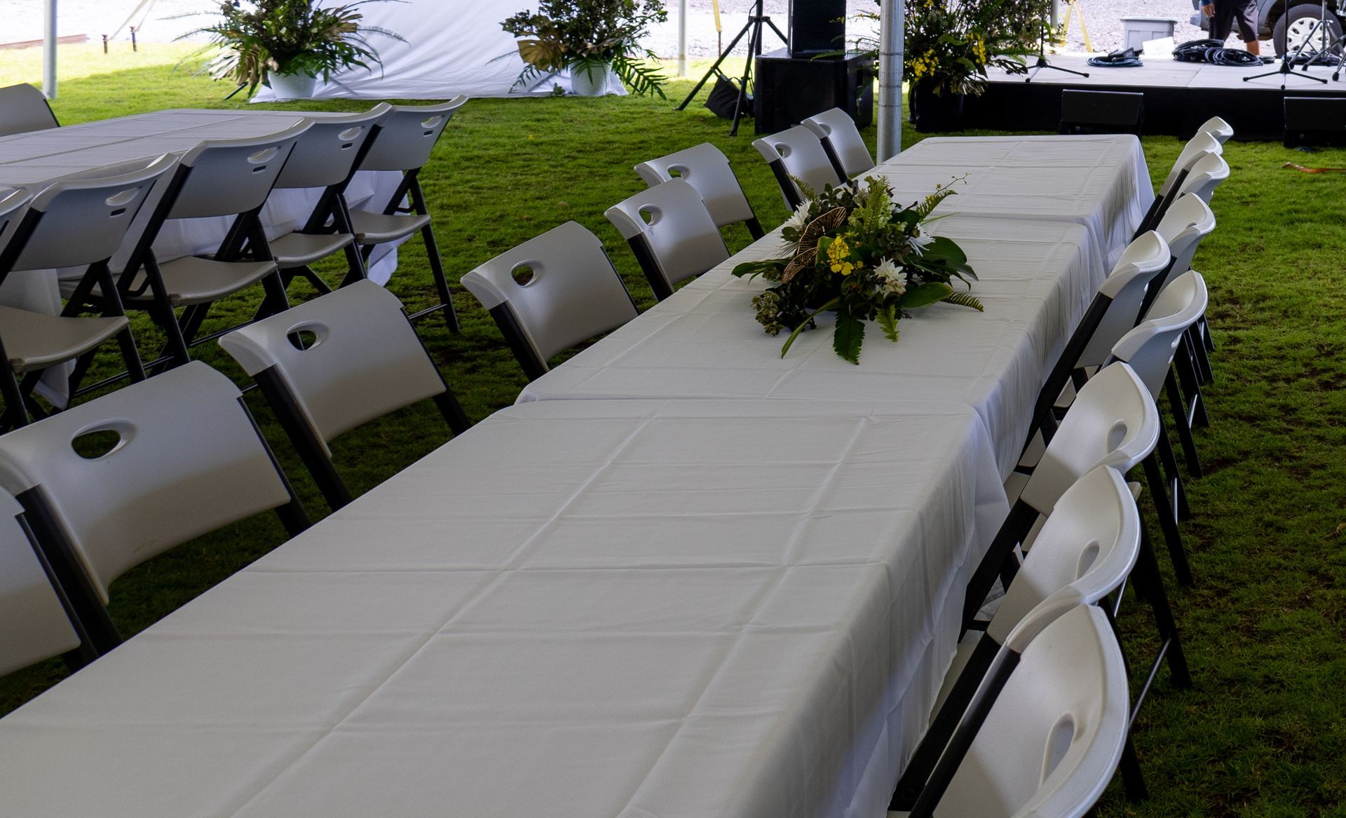 A long table with a white tablecloth and chairs in a tent.