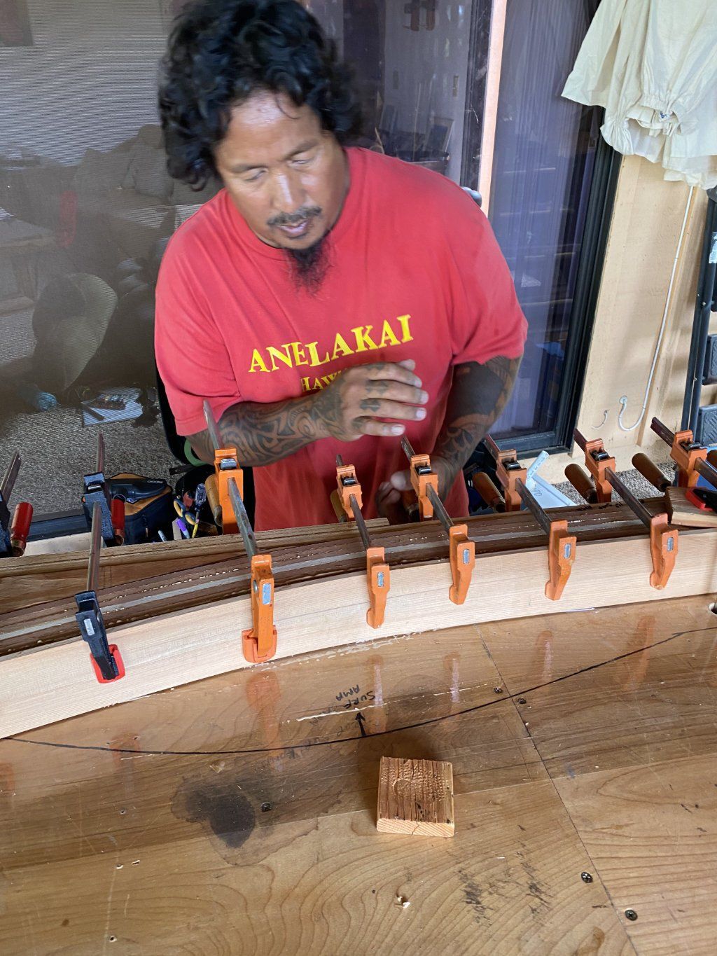 A man in a red shirt is working on a piece of wood