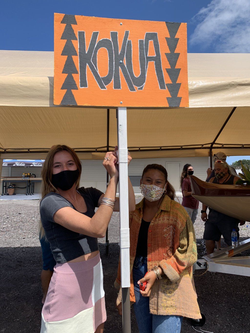Two women wearing masks holding a sign that says kokua
