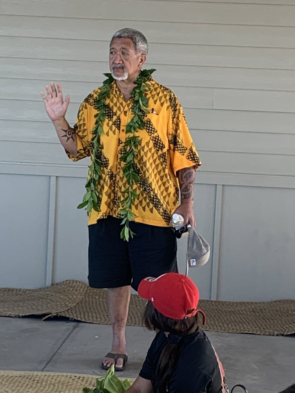 A man wearing a yellow shirt and a lei is standing in front of a white wall.