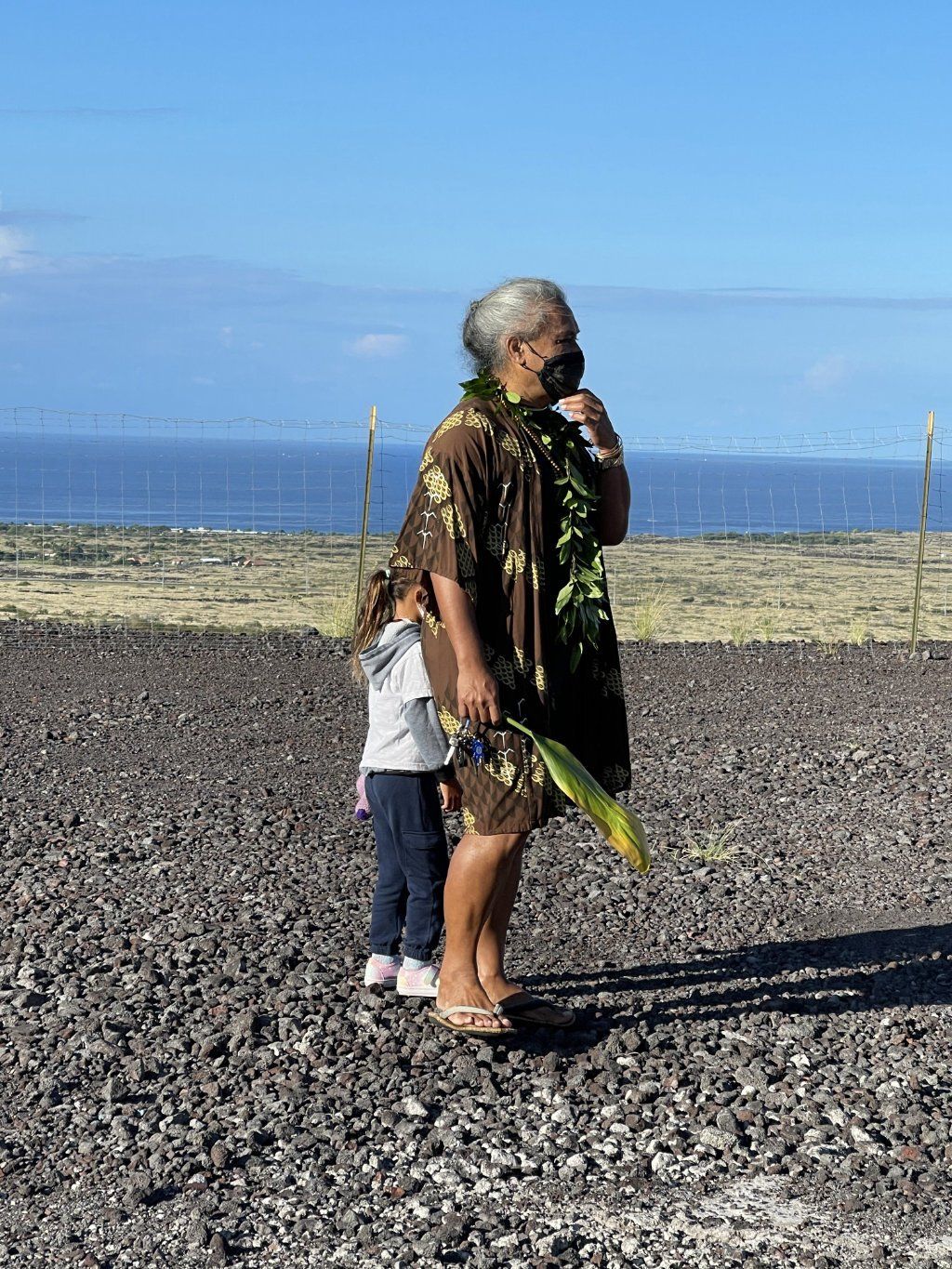 A woman and a little girl are standing on a rocky beach.