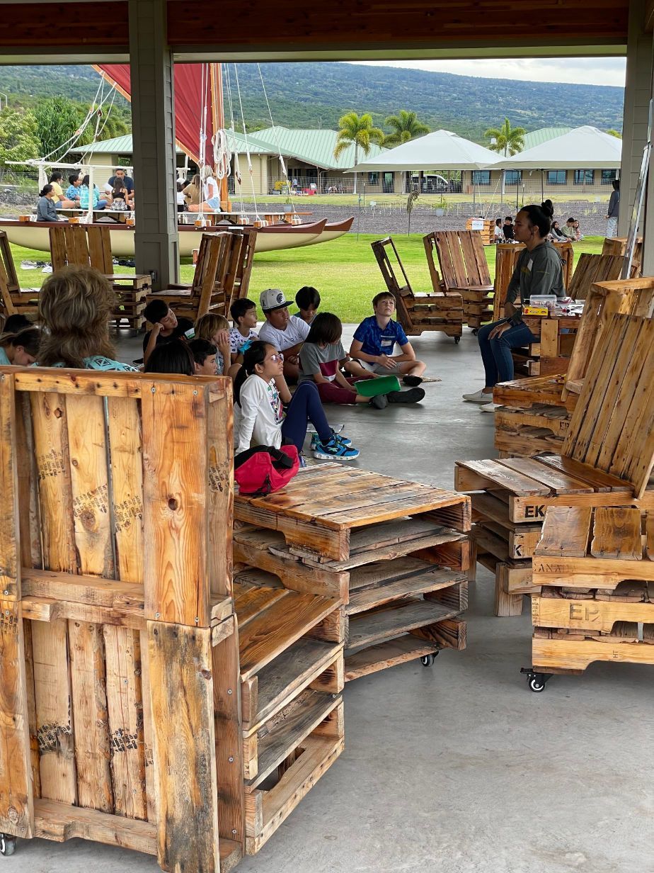 A group of people are sitting in wooden chairs made out of wooden pallets.