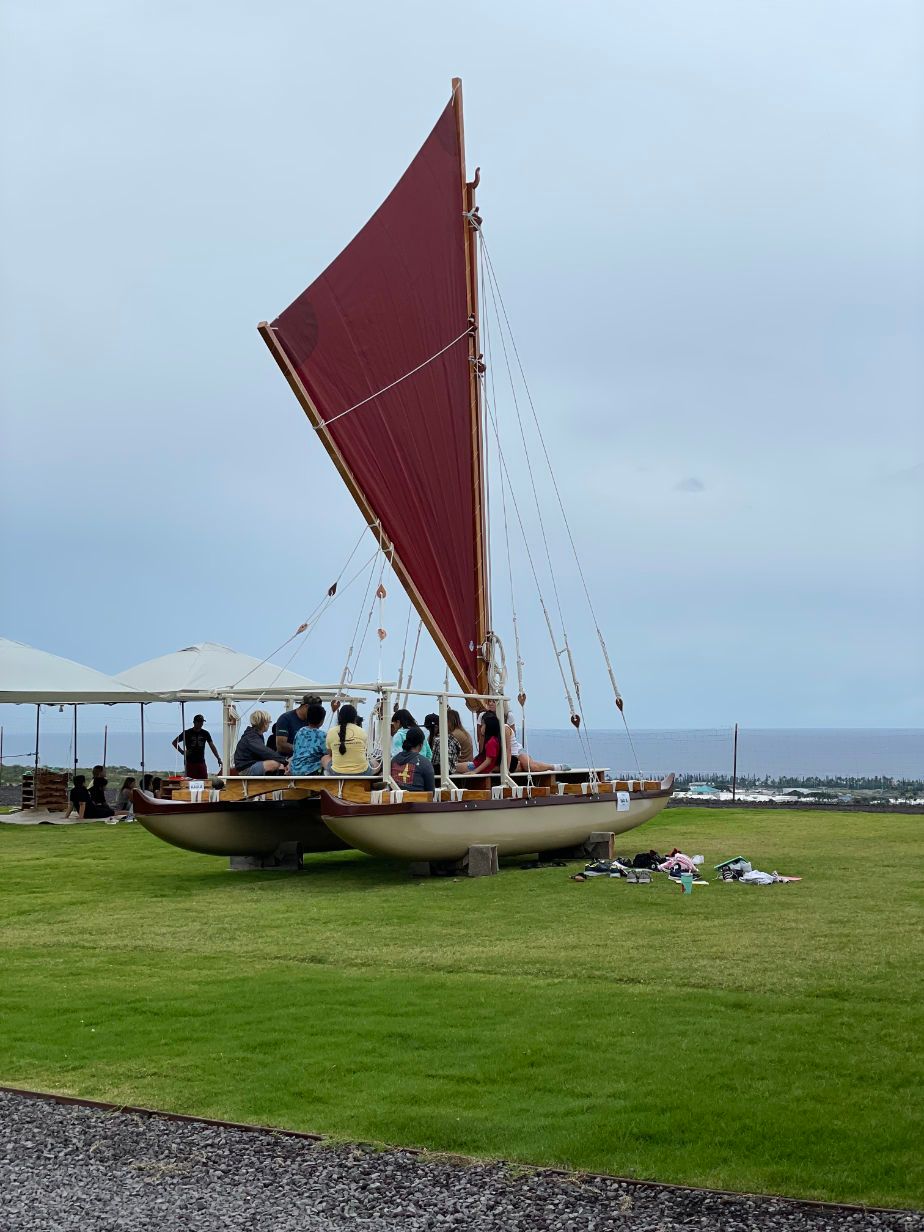 A boat with a red sail is parked in a grassy field