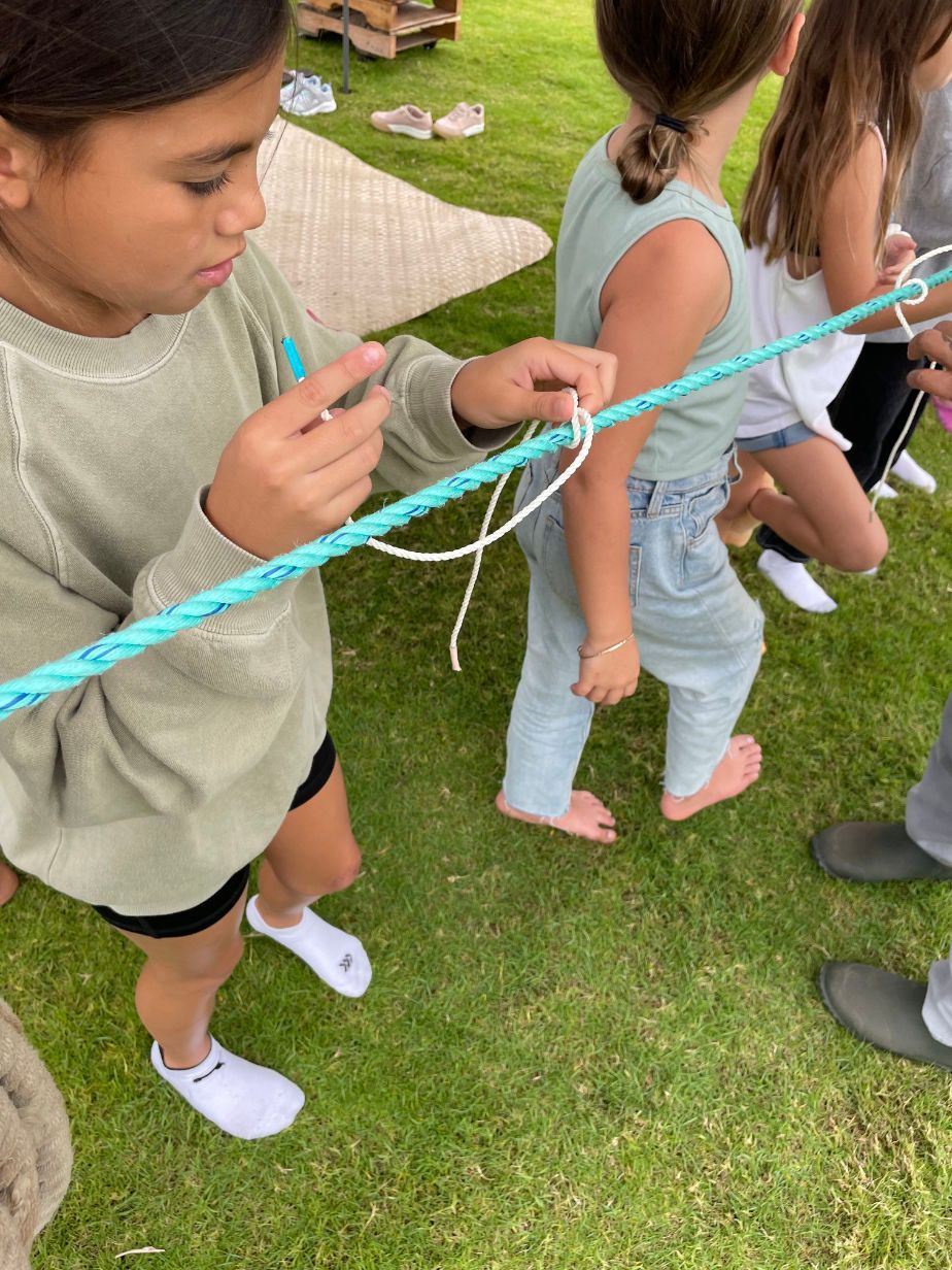 A group of children are playing with a rope in the grass.