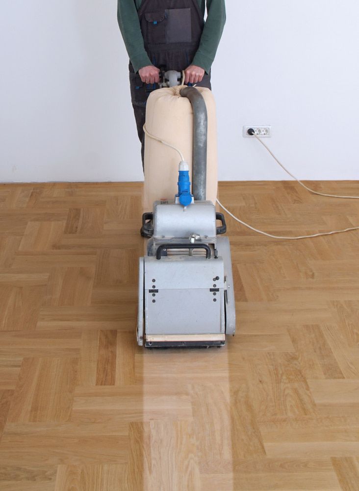 A Man Is Sanding A Wooden Floor With A Machine — Corbett Brothers Flooring In Woy Woy, NSW