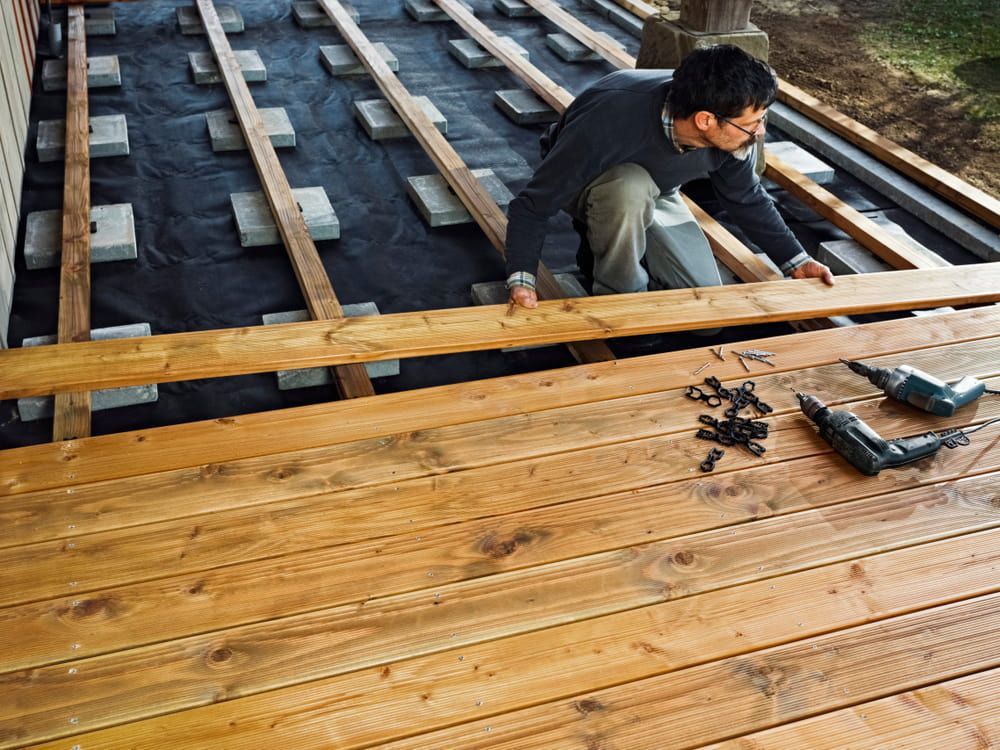 A Man Is Working On A Wooden Deck With A Drill — Corbett Brothers Flooring In Woy Woy, NSW