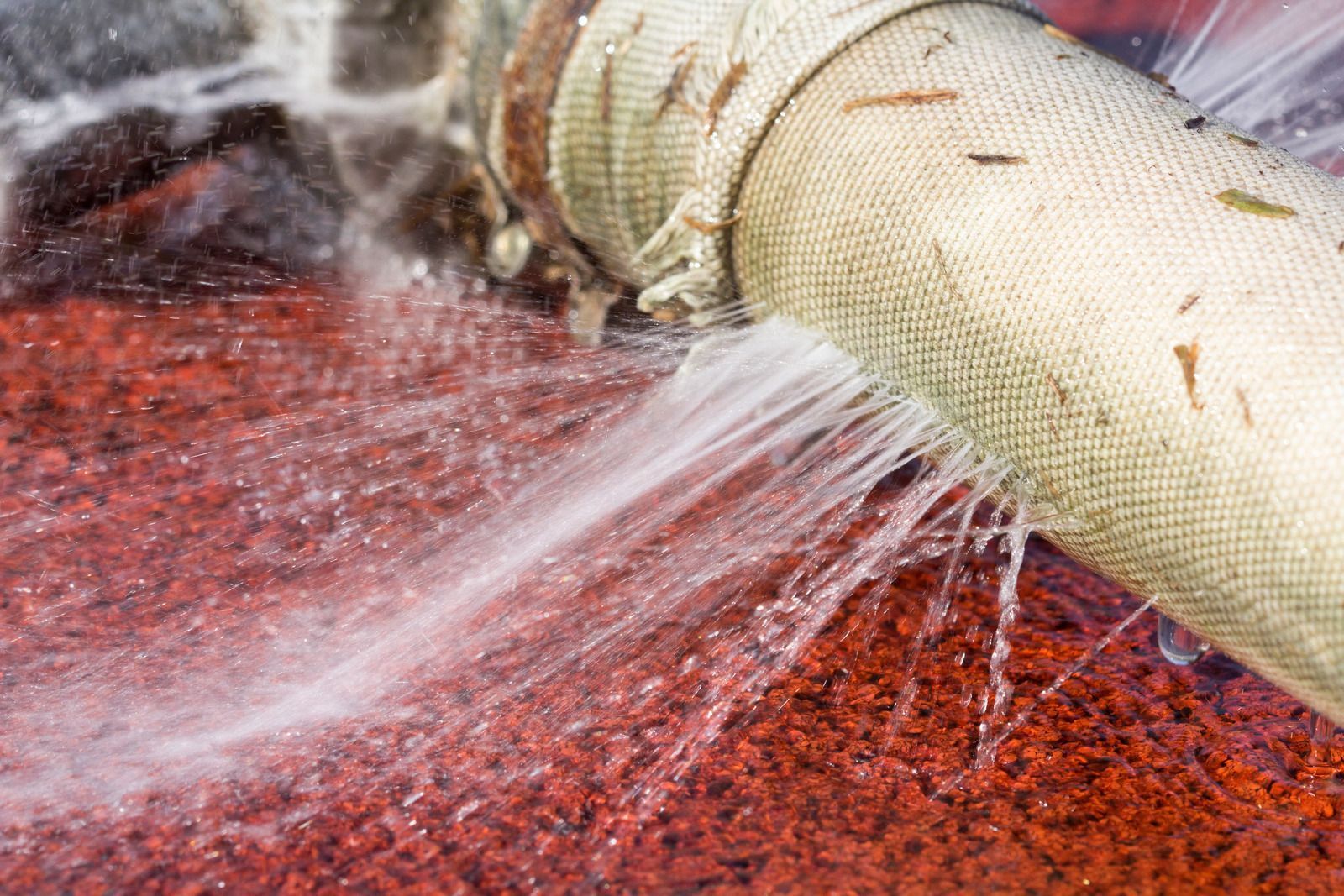 Water gushing from a torn, fabric-covered pipe on a red surface.