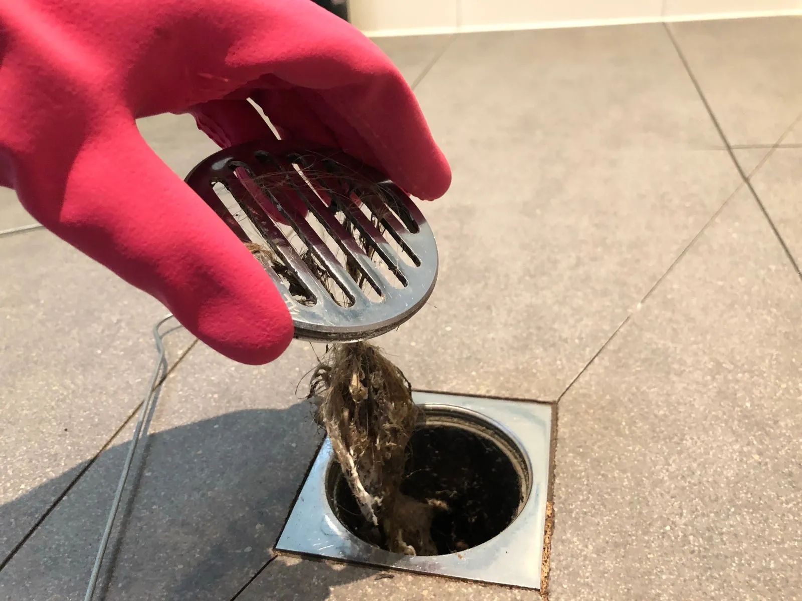 A person wearing red gloves is cleaning a drain with a brush.