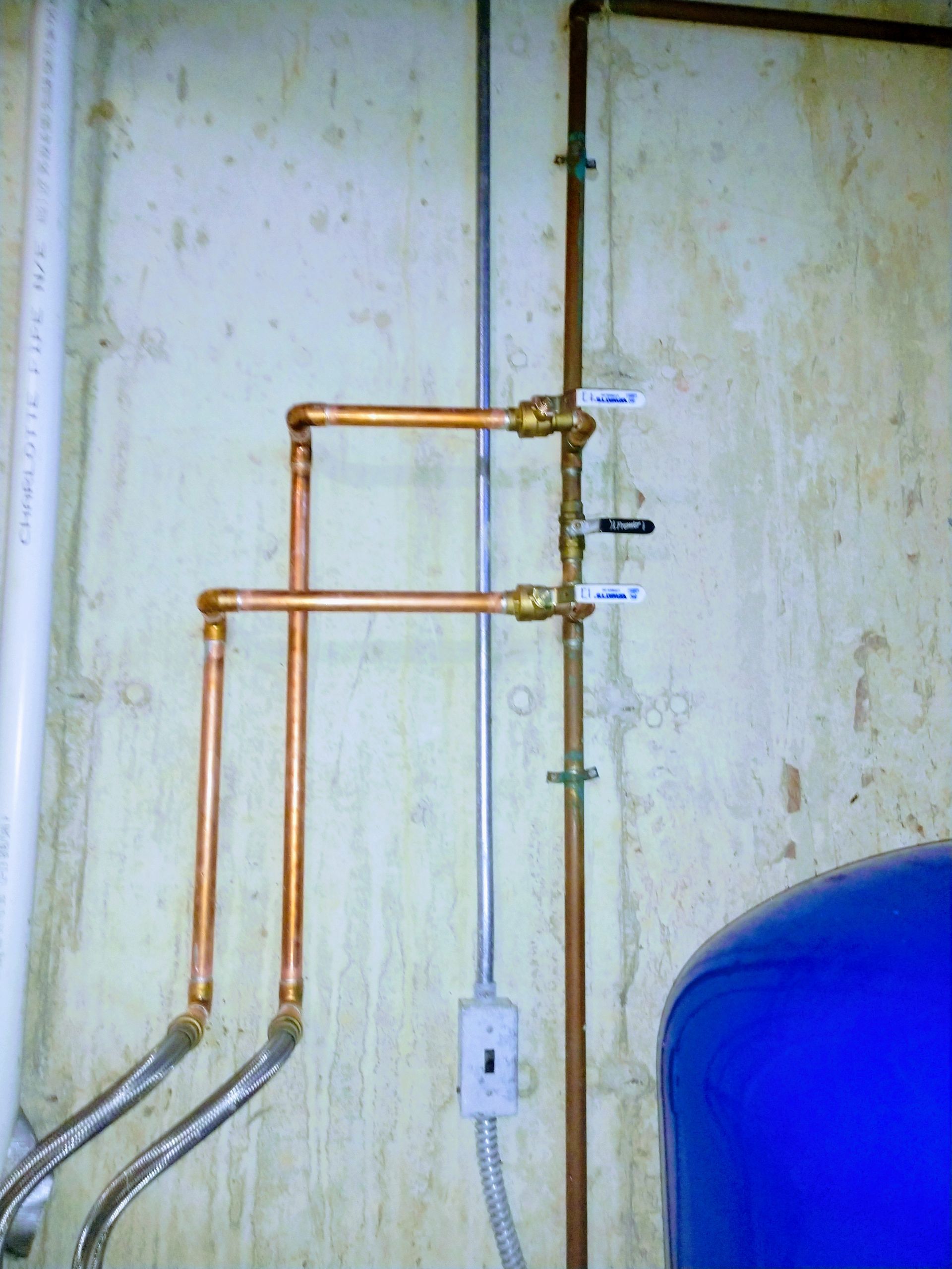 Copper pipes are connected to a wall next to a blue tank.