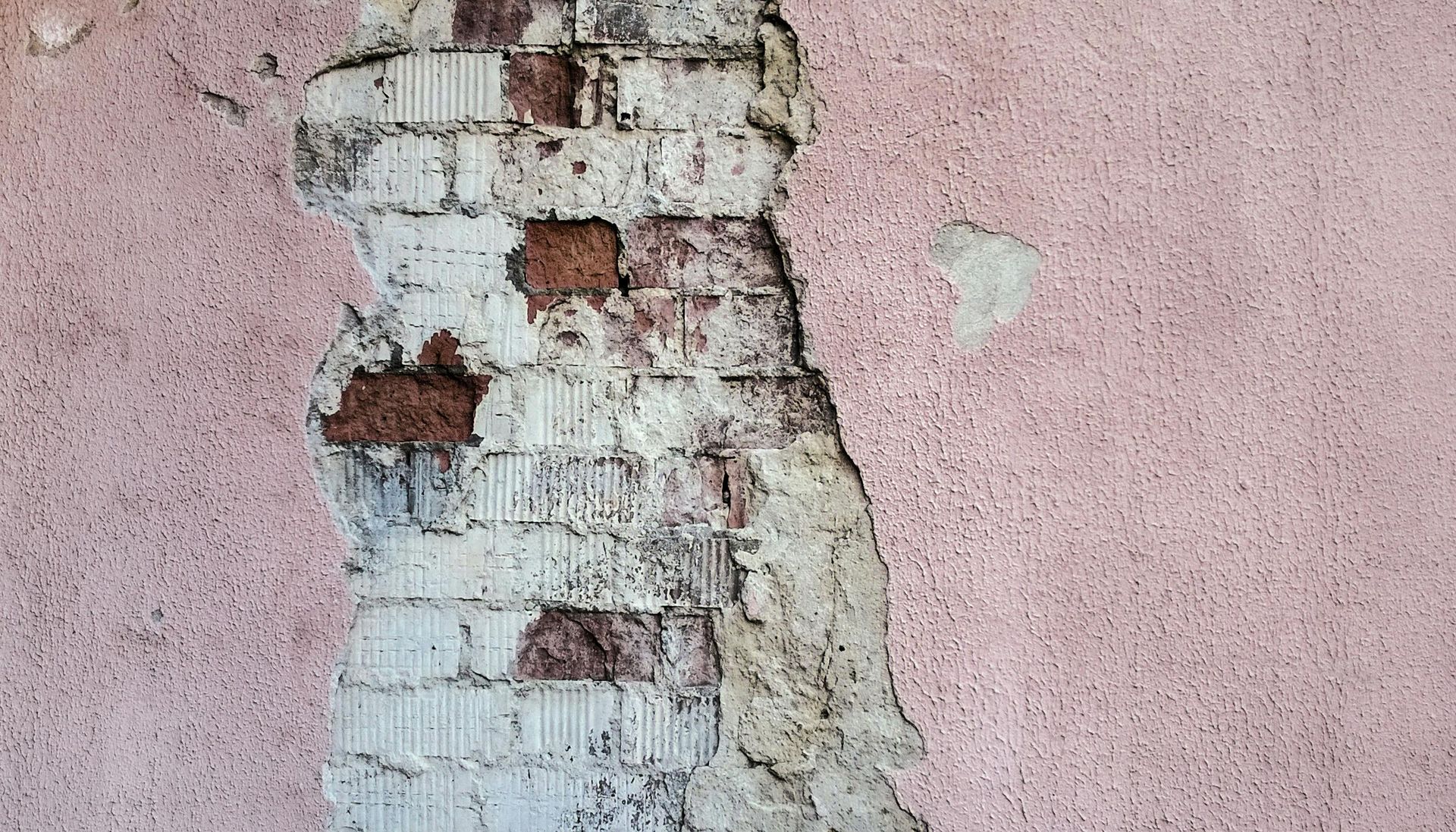 Exposed brick wall section with peeling pink stucco revealing brick and mortar.