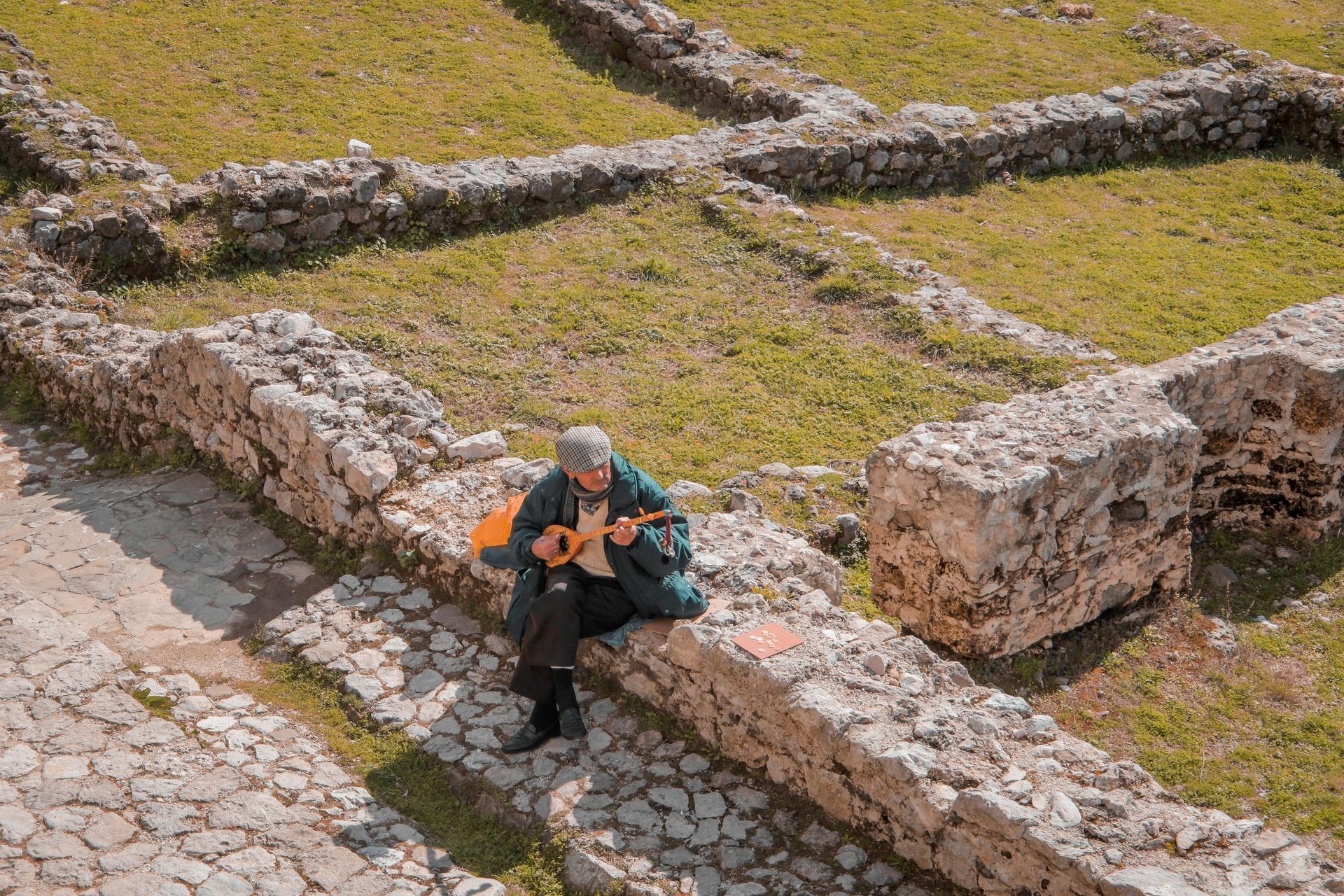 Man playing stringed instrument on stone wall within ancient ruins.