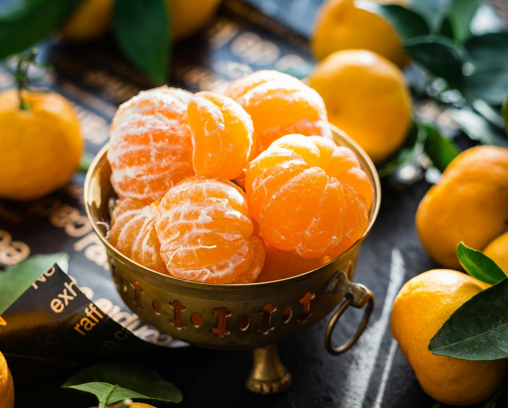 Bowl of peeled orange mandarin orange segments with whole mandarins around it.