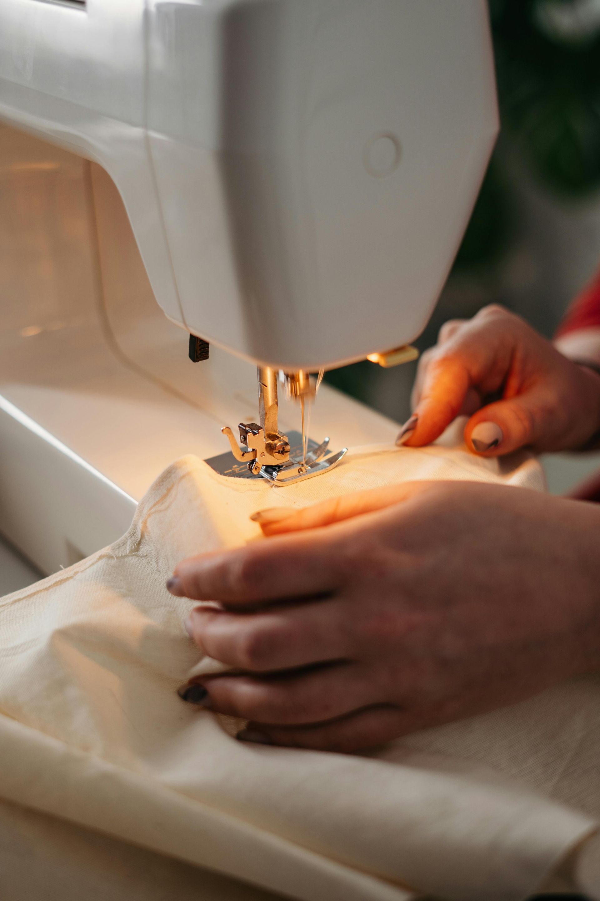 Hands guiding fabric under the needle of a white sewing machine, illuminated by the machine's light.