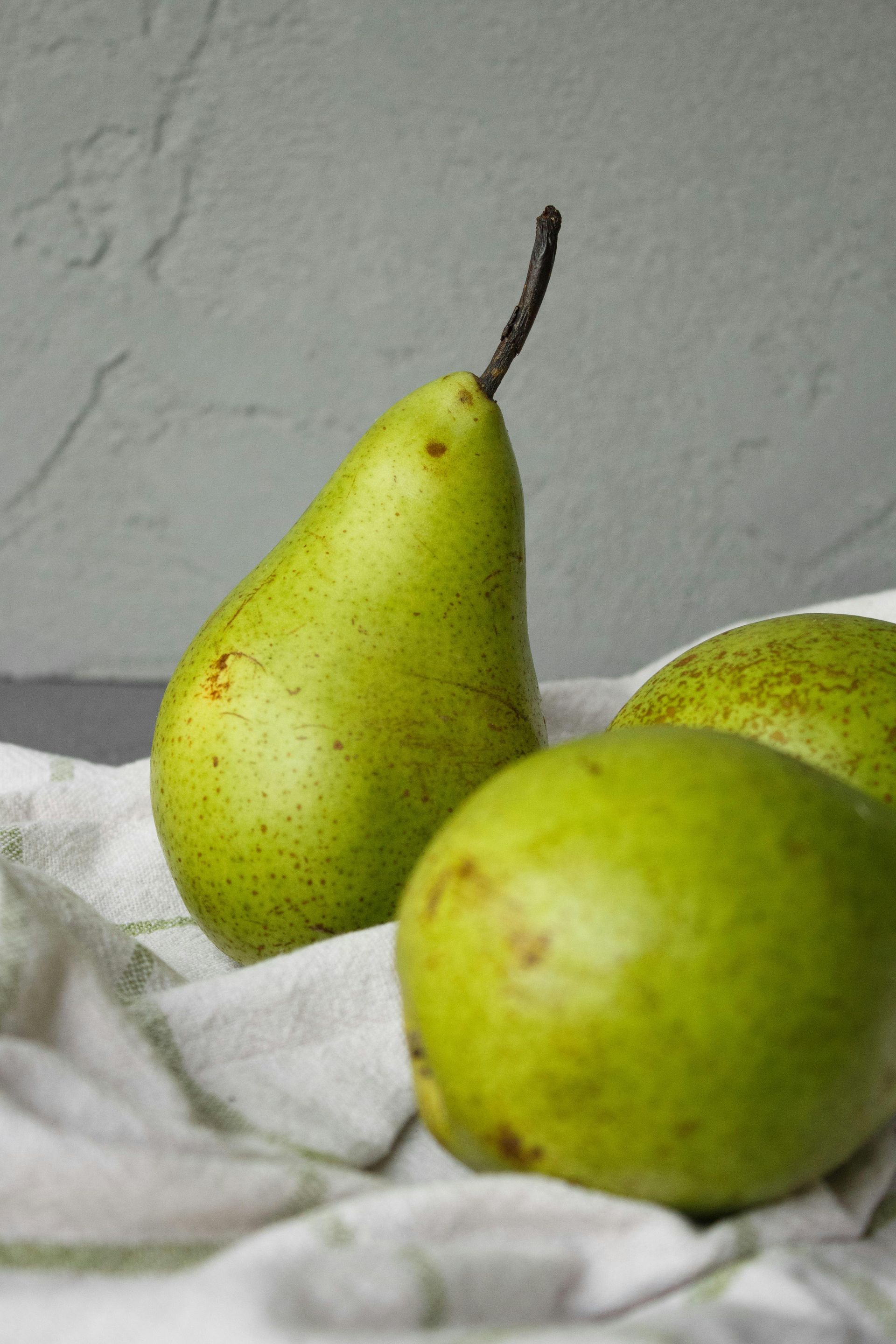Green pears on a white cloth, against a gray background.